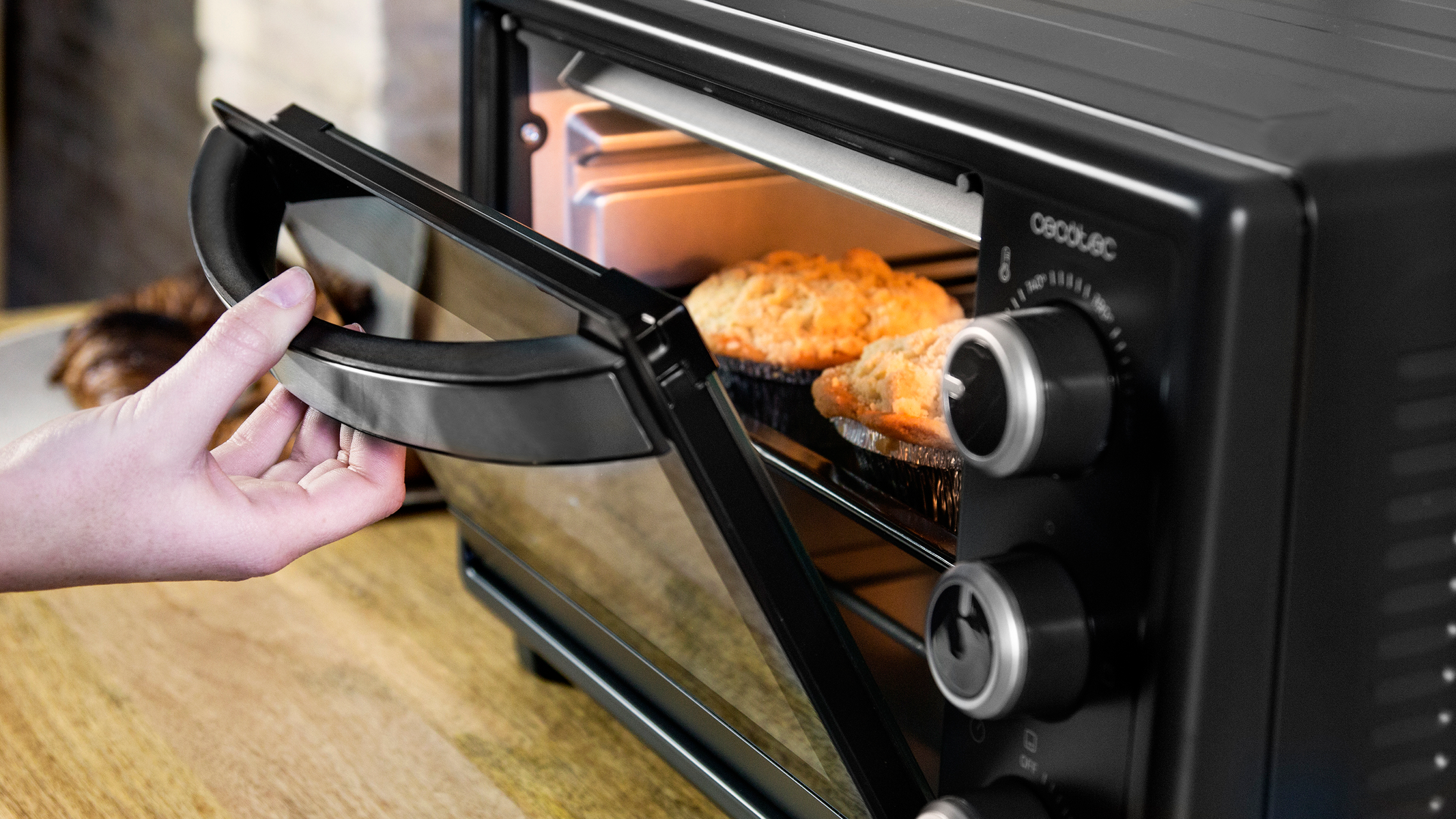 Piekarnik z babeczkami w środku. Ręka otwiera szklane drzwi, aby do nich się dostać.