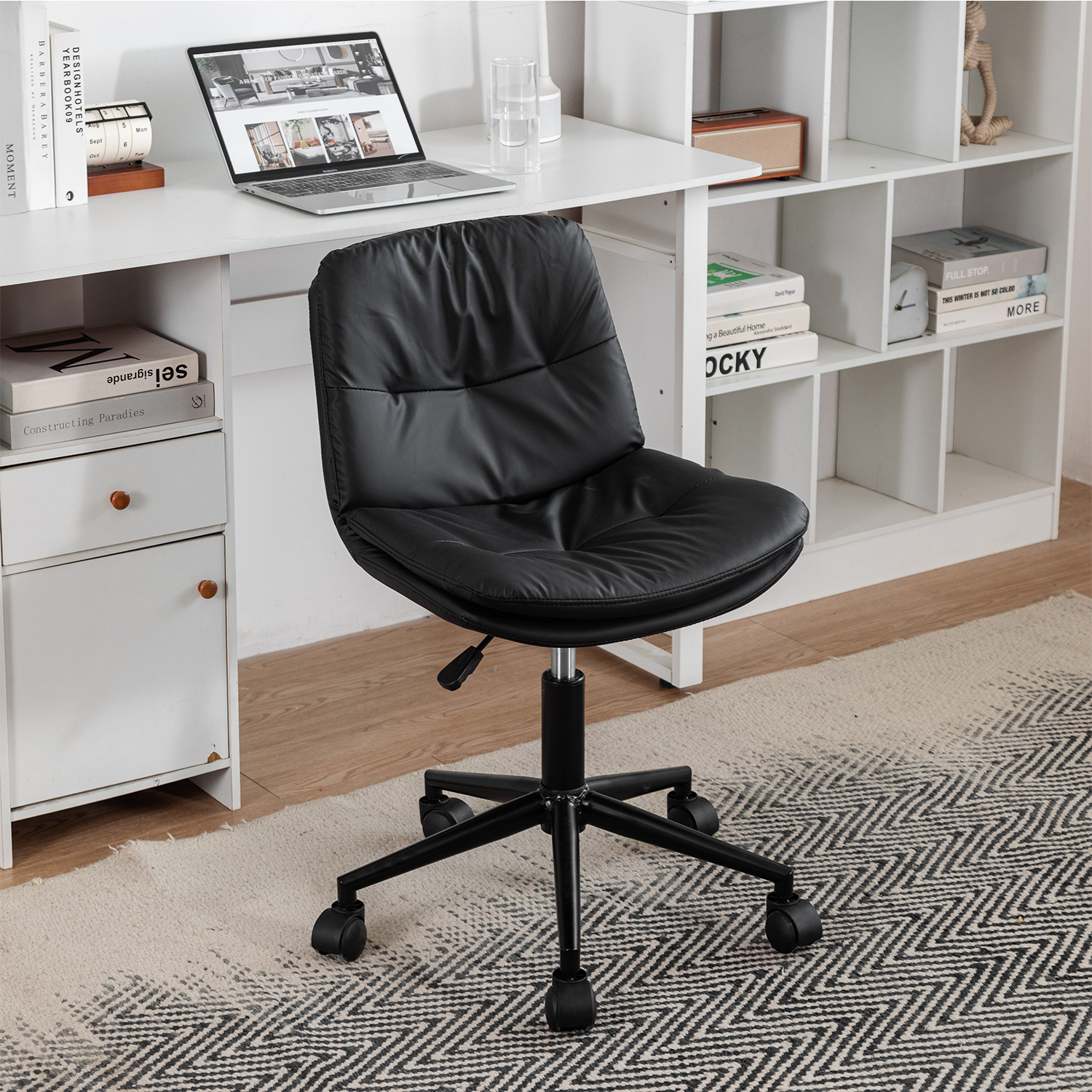 Schwarzer Leder-Bürostuhl auf Rädern, vor einem weißen Schreibtisch mit Laptop und Büchern.