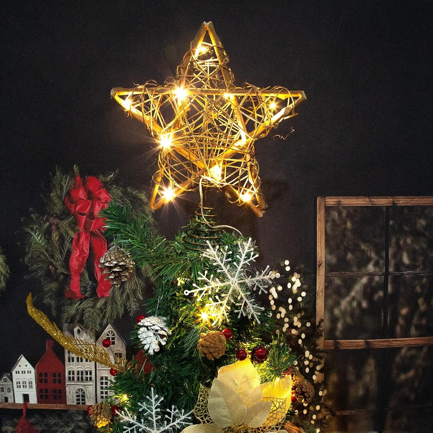 Weihnachtsbaum mit Sternspitze und Dekorationen, Lichtern und kleinen Häusern im Hintergrund.