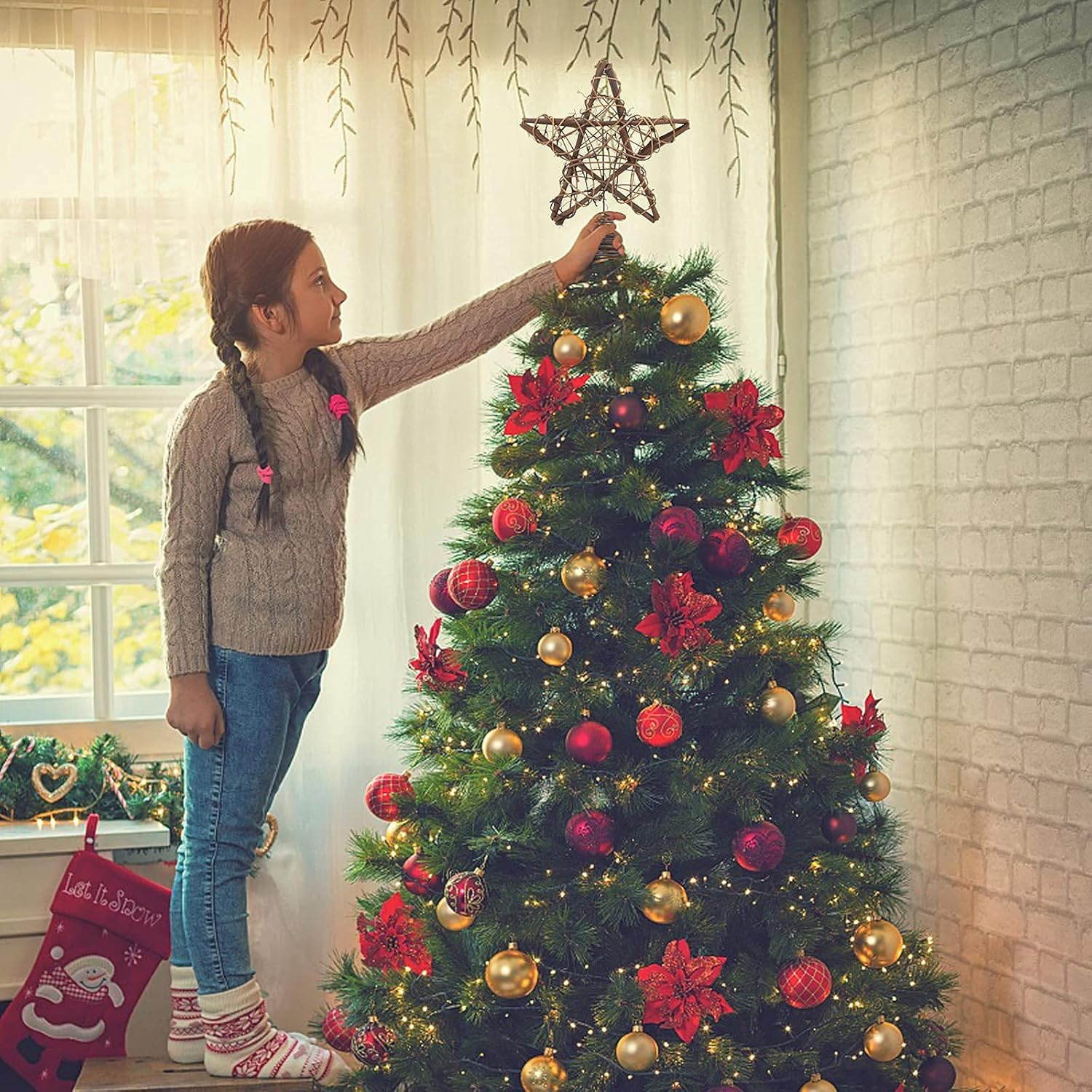 Ein junges Mädchen, das einen Stern auf einen geschmückten Weihnachtsbaum setzt. Die Szene spielt drinnen.