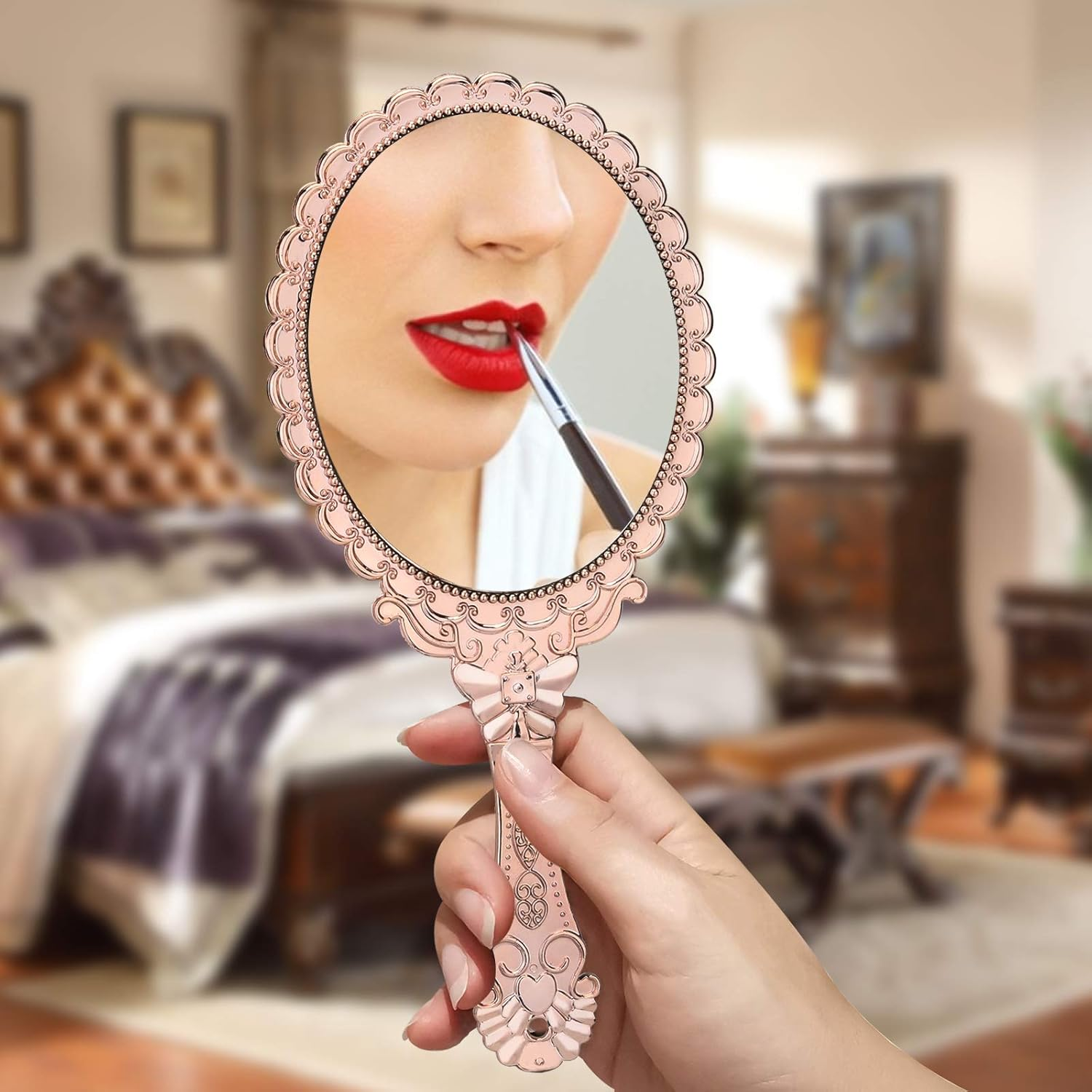 Eine Frau trägt Lippenstift in einem Handspiegel auf. Der Spiegel hat einen rosa Rahmen, Raum im Hintergrund.