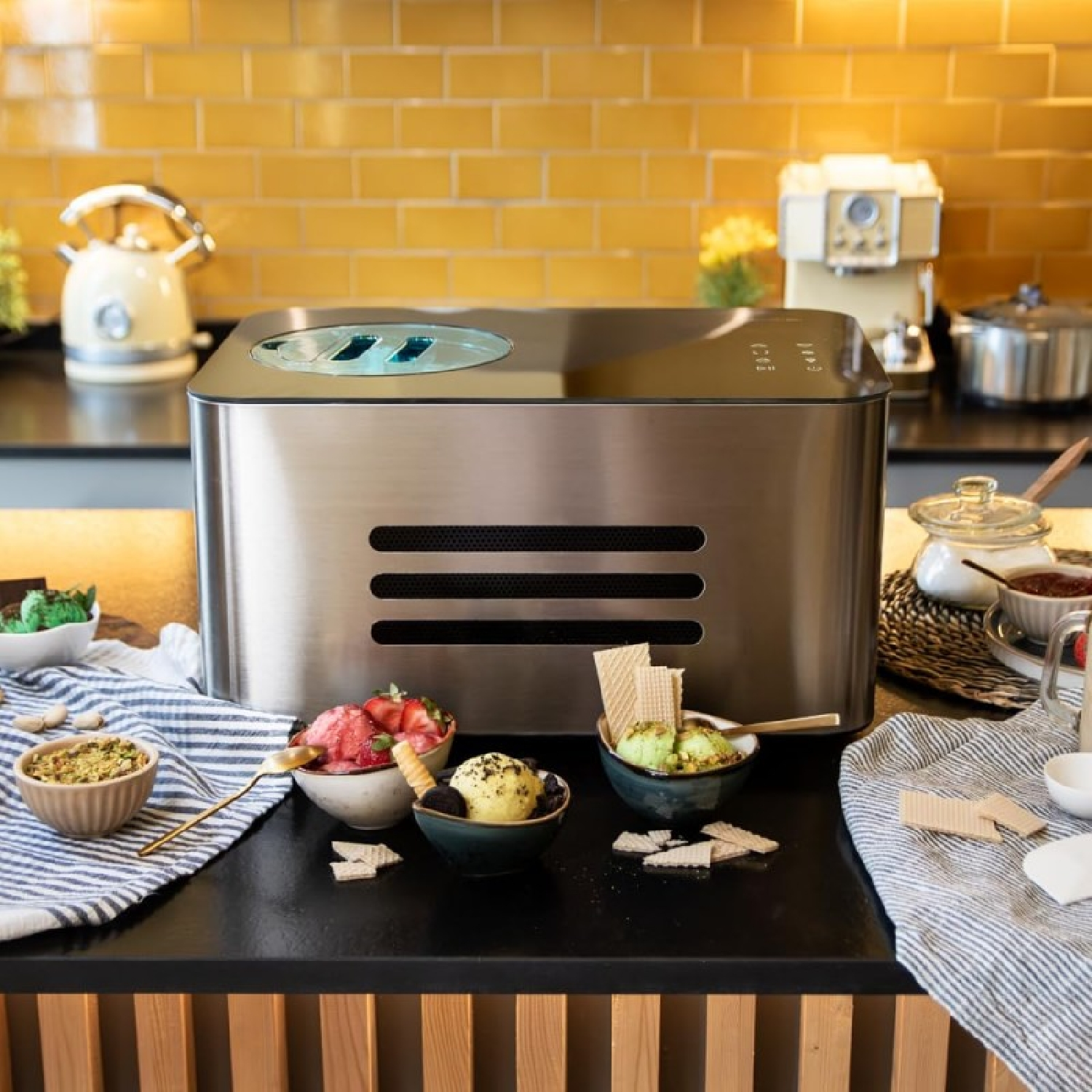 Maszyna do lodów z miseczkami lodów, dodatkami i rożkami waflowymi na ladzie.