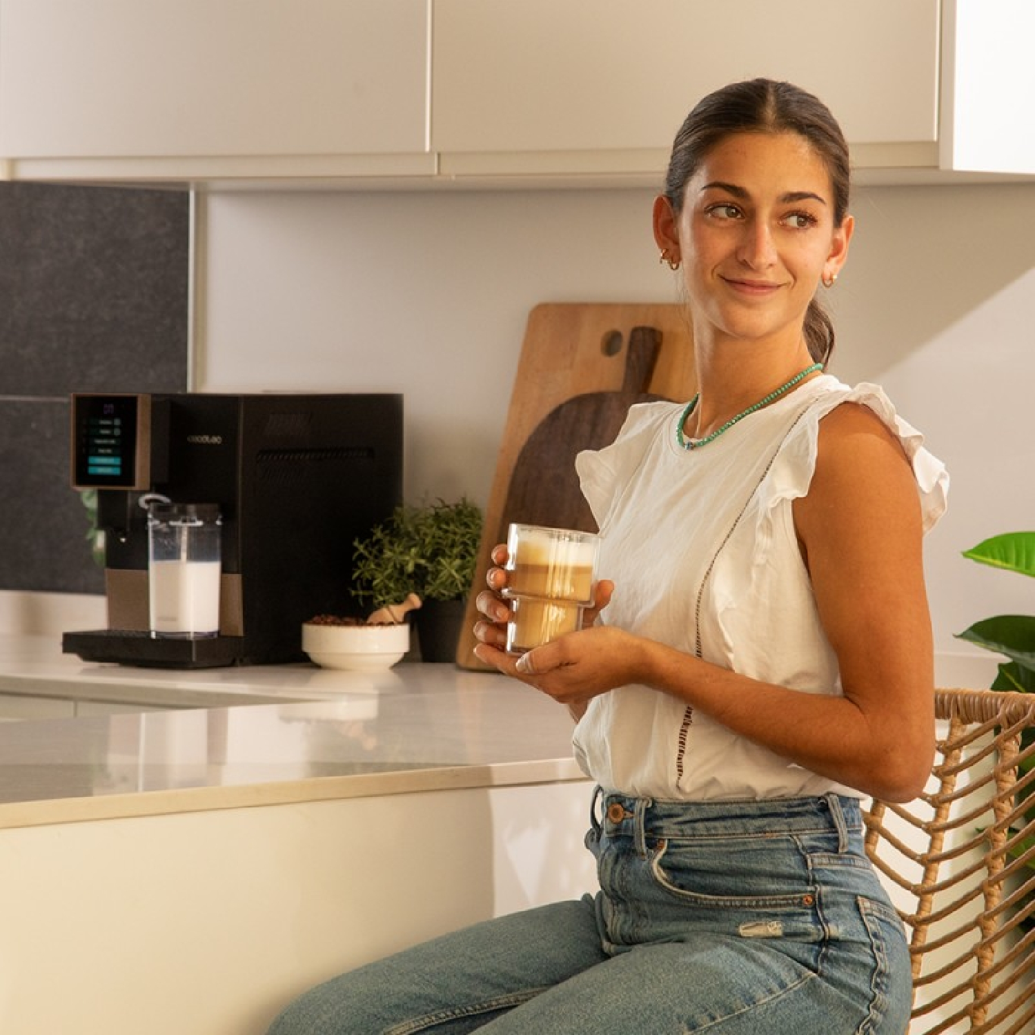 Una donna in cucina, che tiene in mano una bevanda al caffè, guarda verso destra.