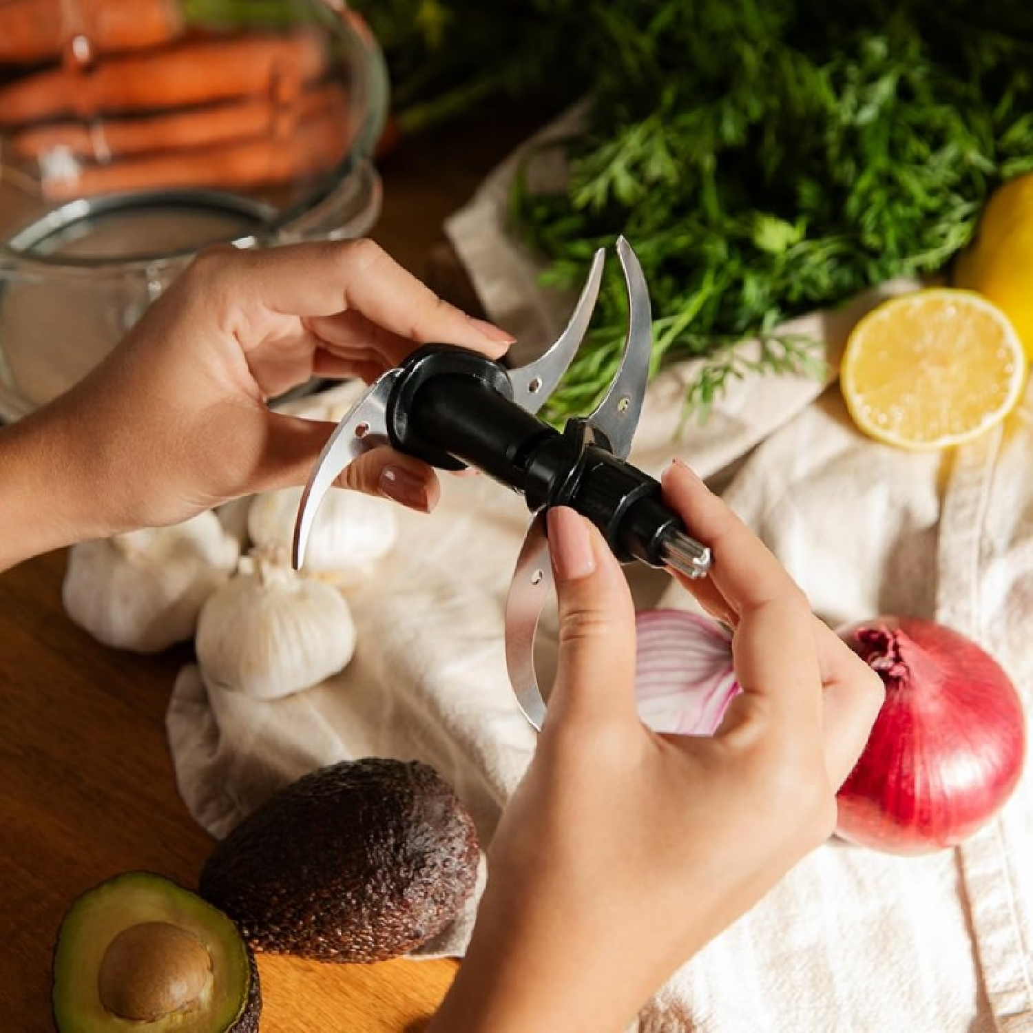 Mani che tengono una lama nera di un robot da cucina sopra verdure, con cipolle, aglio e avocado.