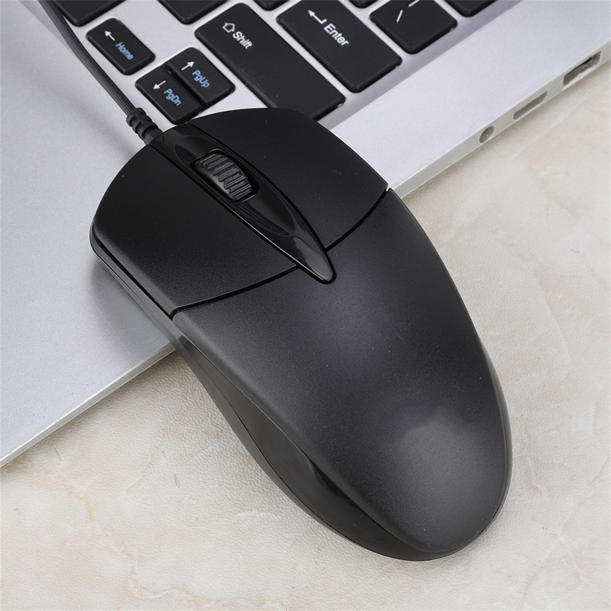 Schwarze Maus auf einem silbernen Laptop. Die Maus hat ein Scrollrad. Beige marmorierter Hintergrund.