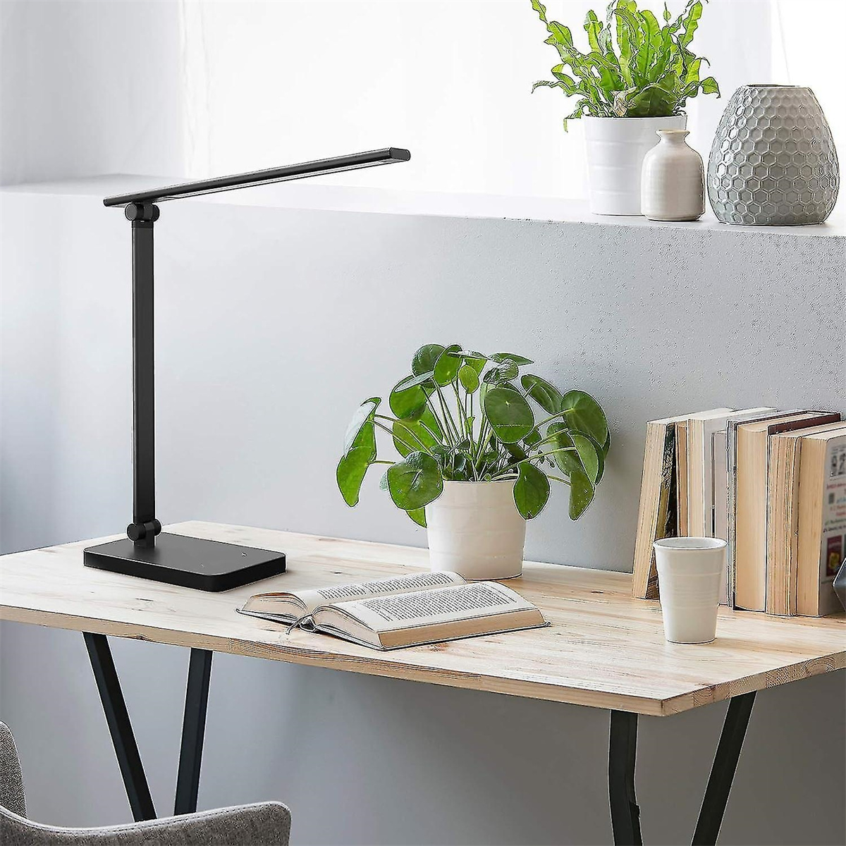 Eine schwarze Schreibtischlampe auf einem Holzschreibtisch mit Pflanzen und einem Buch.