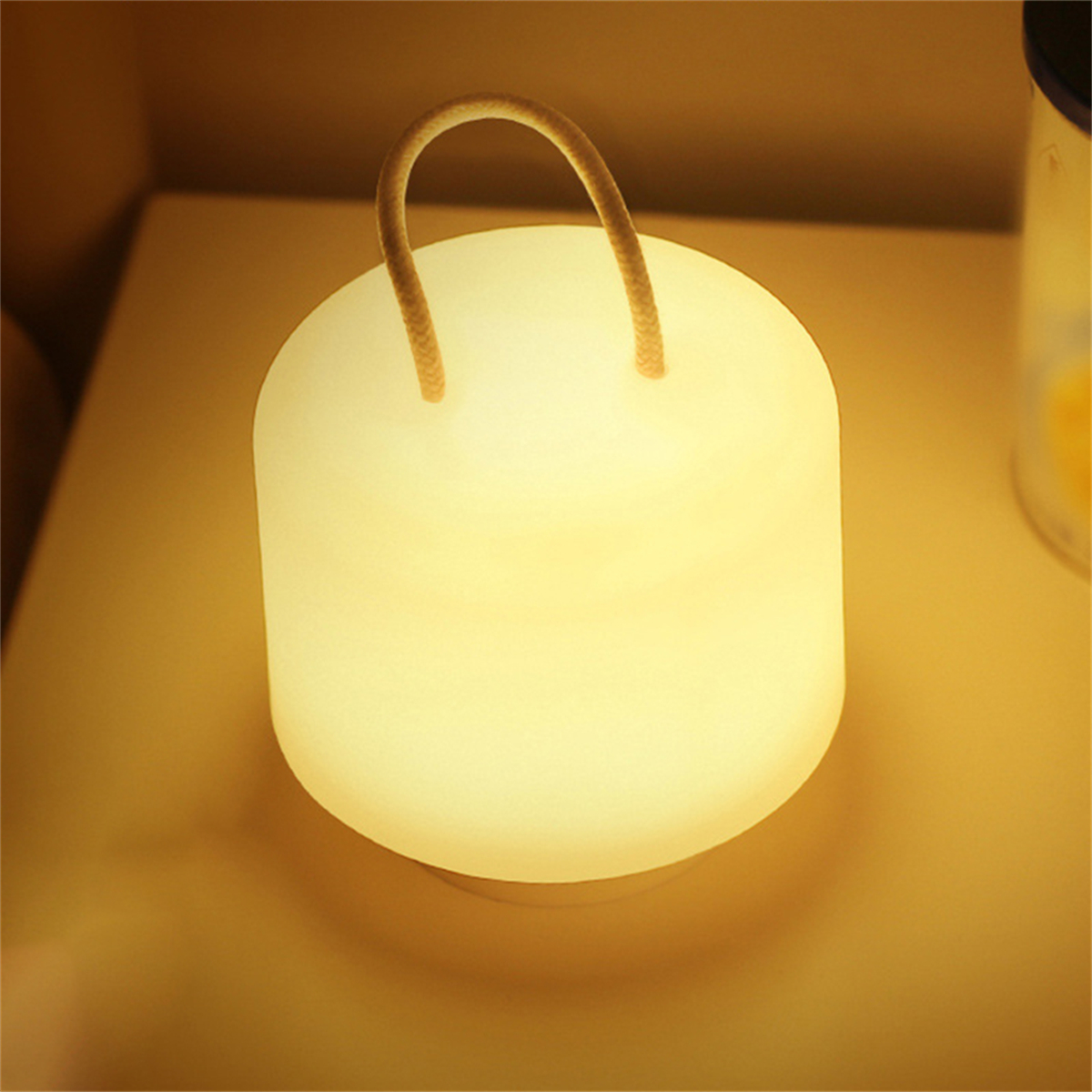 Glühende weiße Lampe auf Holzoberfläche. Die Lampe hat einen hellbraunen Seilgriff.