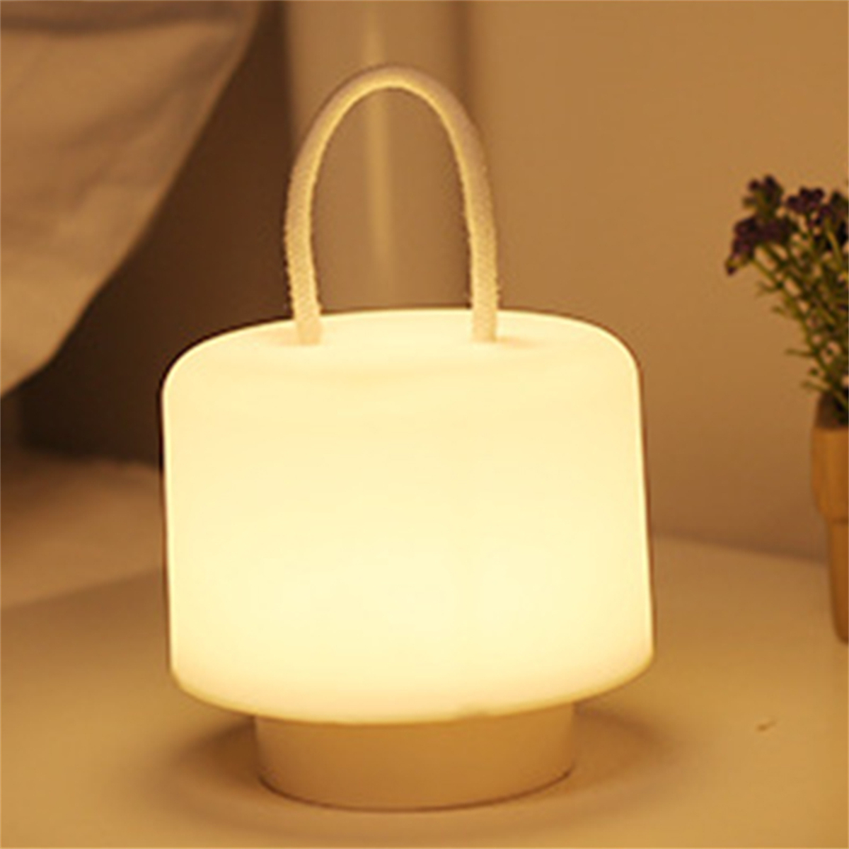 Ein leuchtendes, zylindrisches Nachtlicht mit Griff, das auf einem Nachttisch steht. Das Licht strahlt einen weichen, warmen Schein aus.