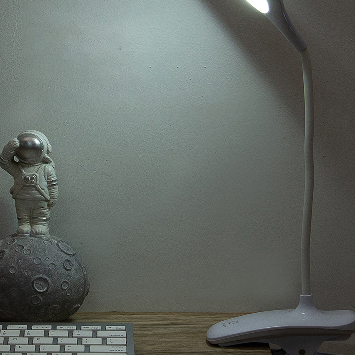 Eine weiße Schreibtischlampe mit einer Astronautenstatue auf einem mondförmigen Objekt. Weißer Hintergrund.