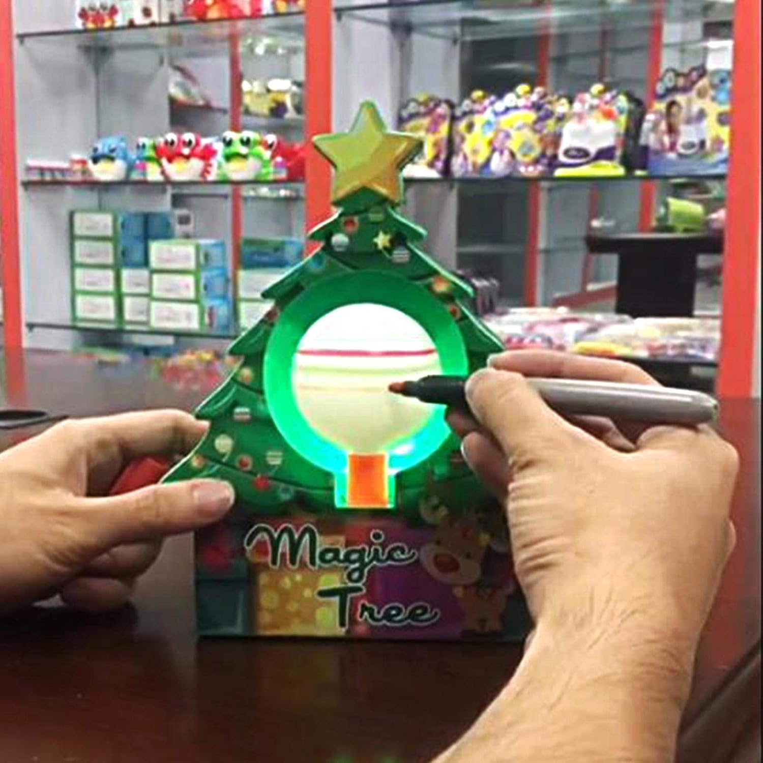 Person zeichnet mit einem Marker auf einen weihnachtsbaumförmigen Lichtprojektor, Spielzeug im Hintergrund.