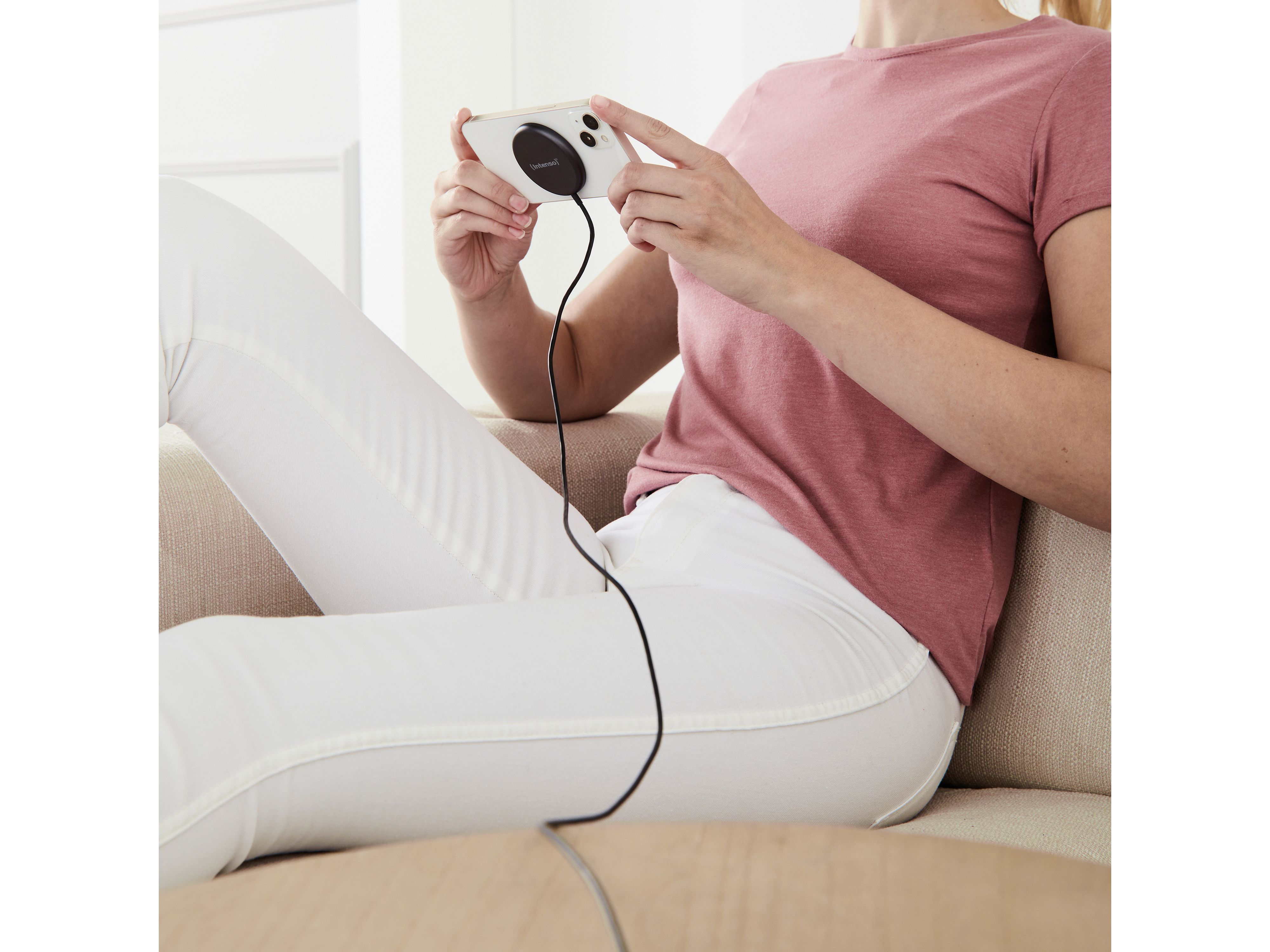 Eine Person in weißer Hose und rosa Oberteil sitzt und hält ein Telefon mit schwarzem Kabel.