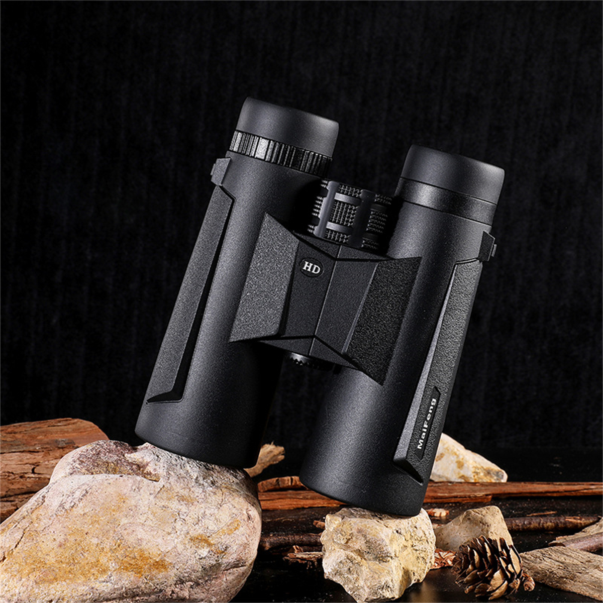 Schwarzes Fernglas mit HD-Aufdruck auf Felsen, vor dunklem Hintergrund mit Tannenzapfen.