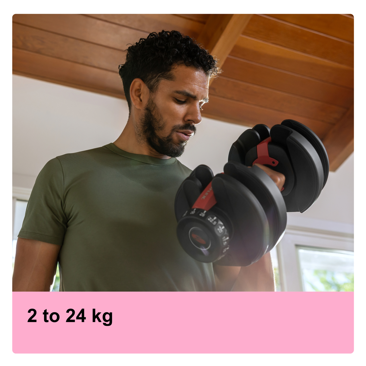 A man in a green shirt lifting a black adjustable dumbbell in a home setting.