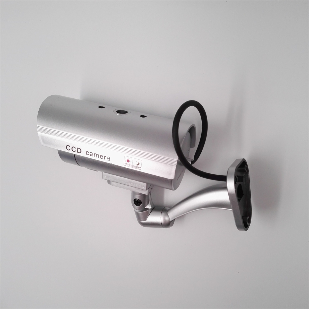 Eine silberne CCD-Kamera, an einer Wand montiert, mit gebogenem Arm, schwarzem Kabel und weißem Hintergrund.
