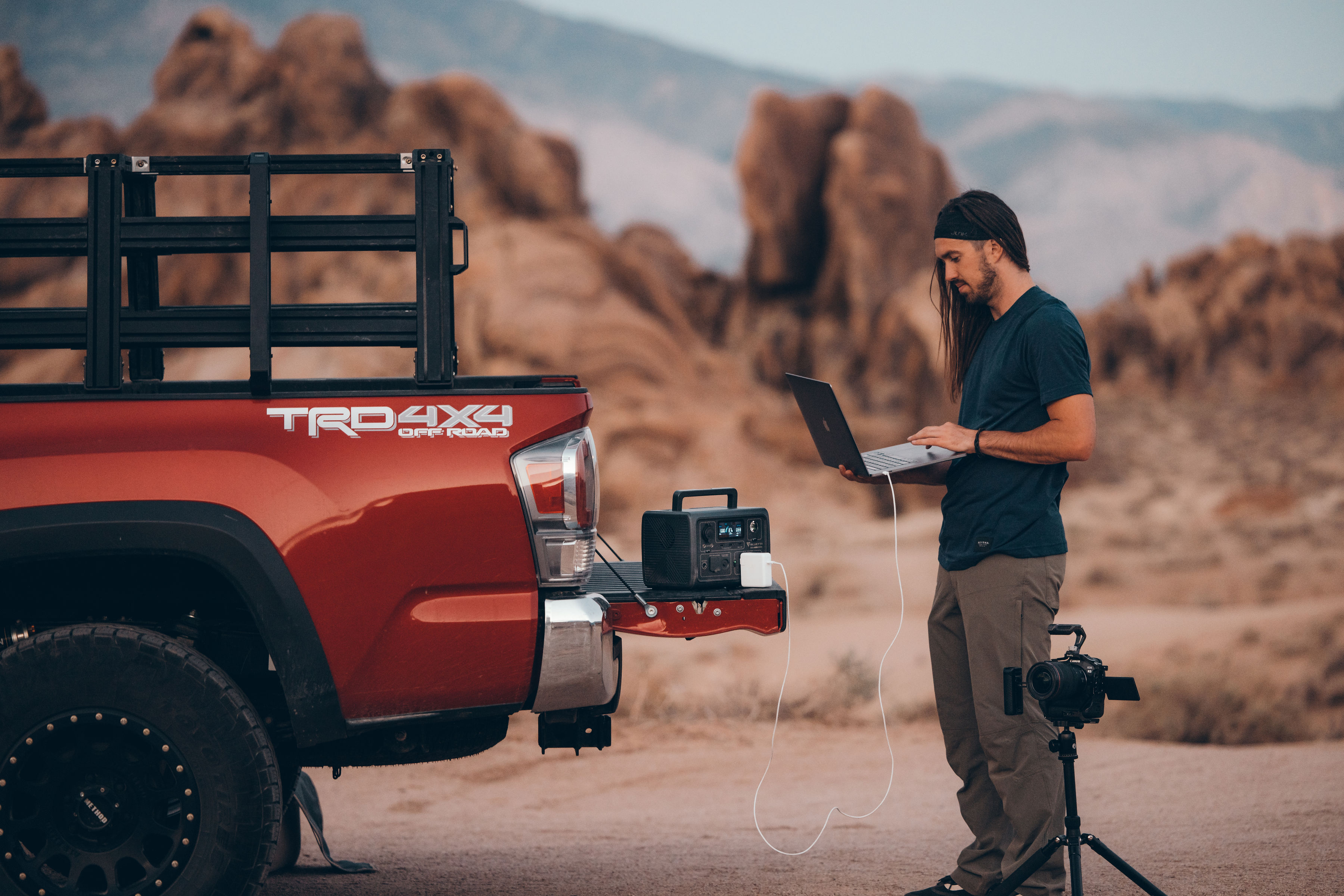 Mężczyzna pracuje na laptopie w pobliżu ciężarówki, z przenośną stacją zasilania na pace.