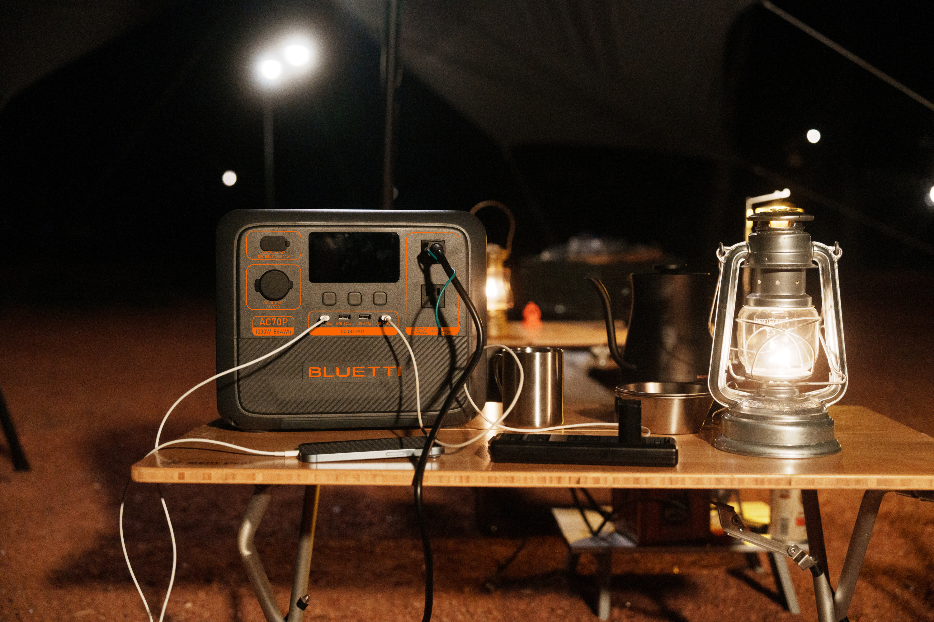 Scena kempingowa z elektrownią, latarnią i innymi przedmiotami na drewnianym stole w nocy.
