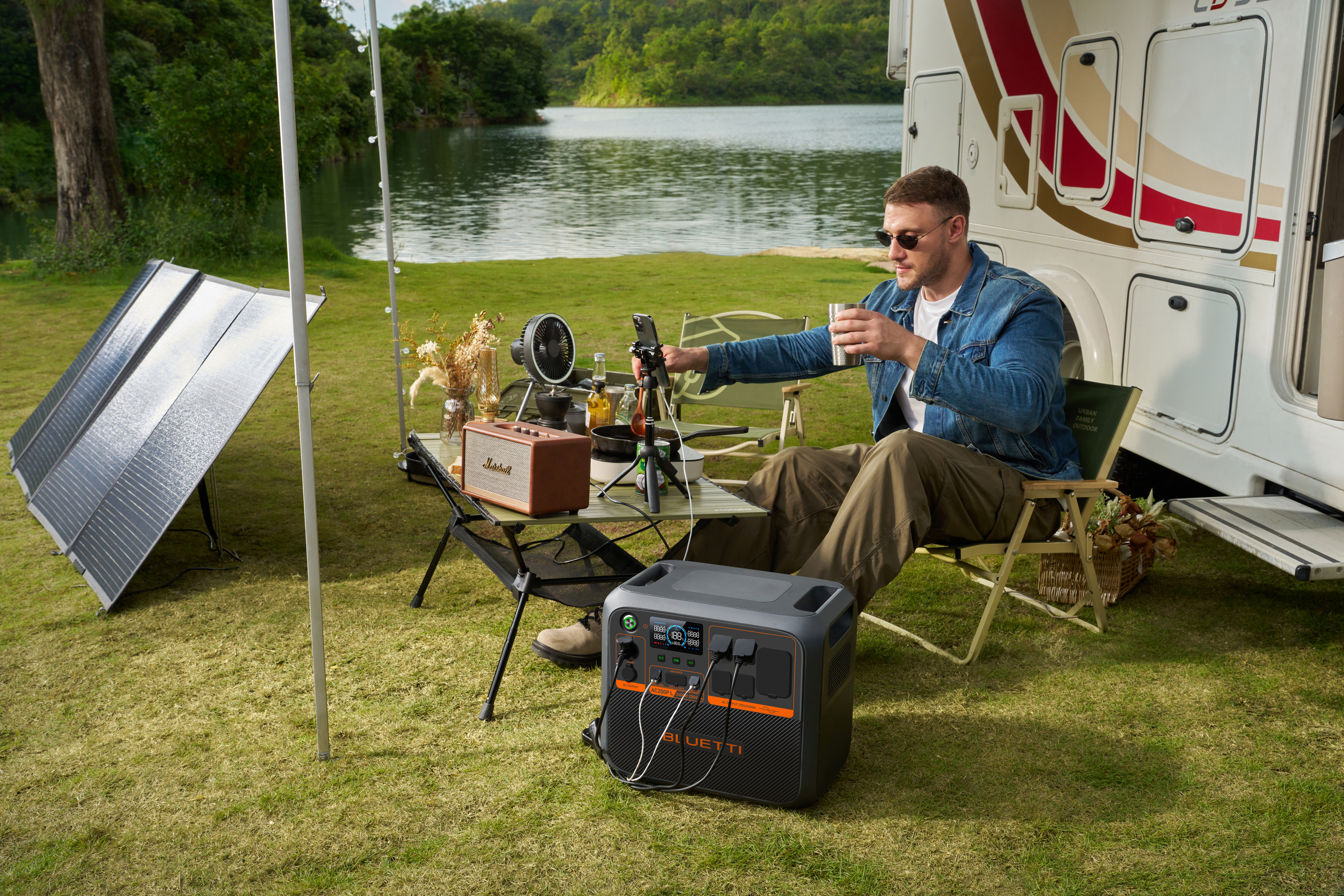 Mężczyzna biwakuje obok kampera. Siedzi przy stole, korzysta z telefonu i ma stację zasilania.