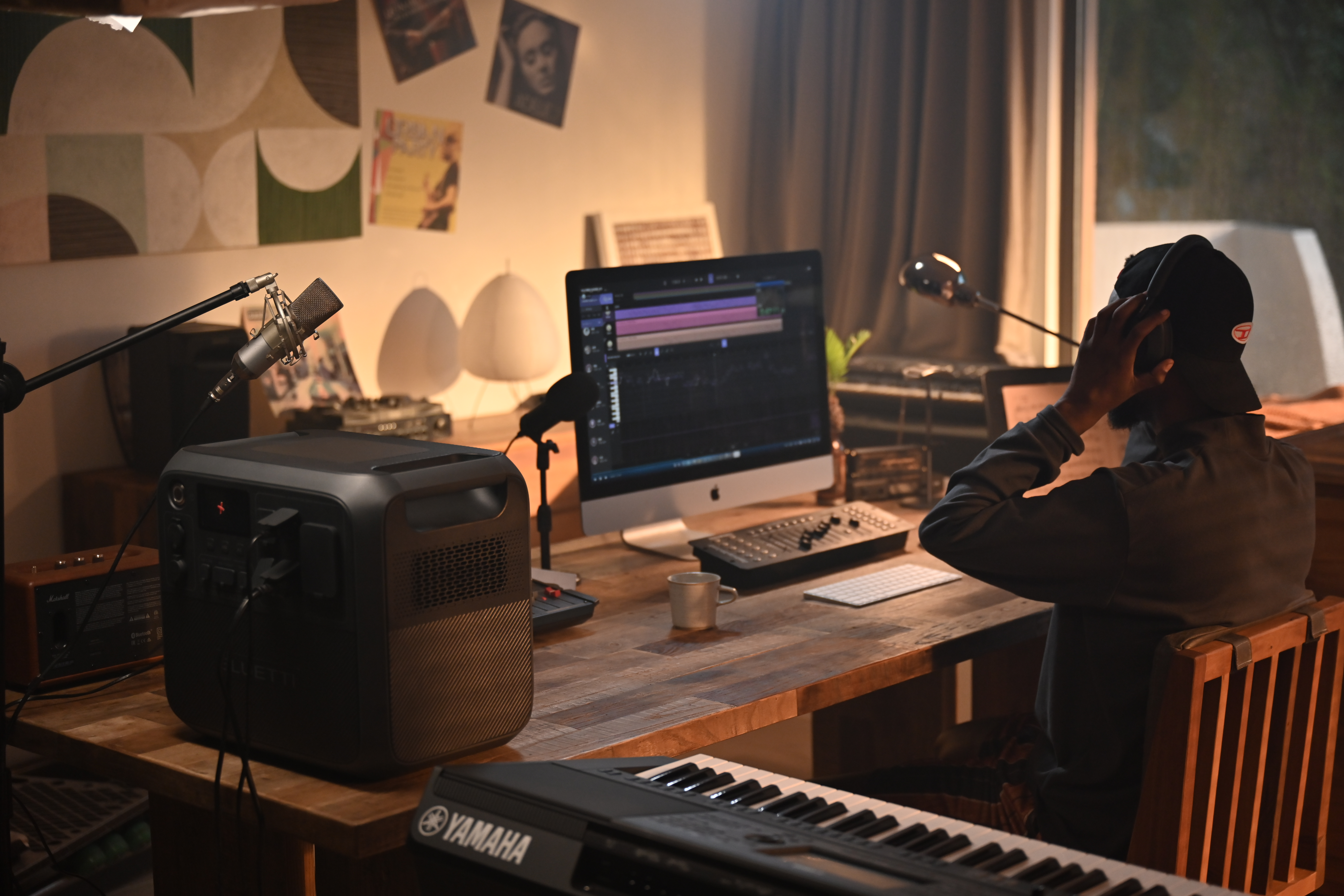 Osoba w studio muzycznym używająca komputera, klawiatury i sprzętu audio.