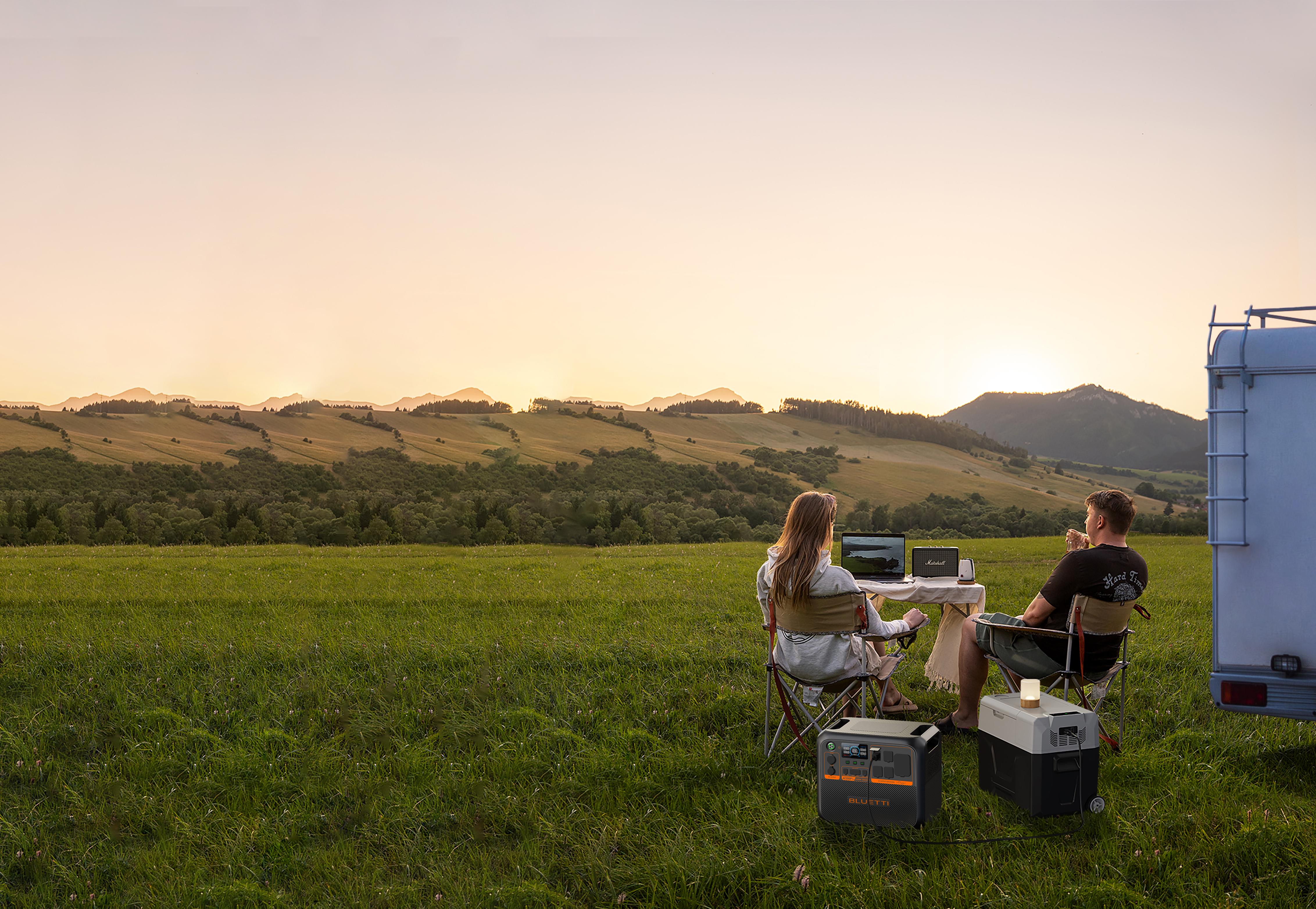 Para na polu z laptopem i sprzętem kempingowym o zachodzie słońca.