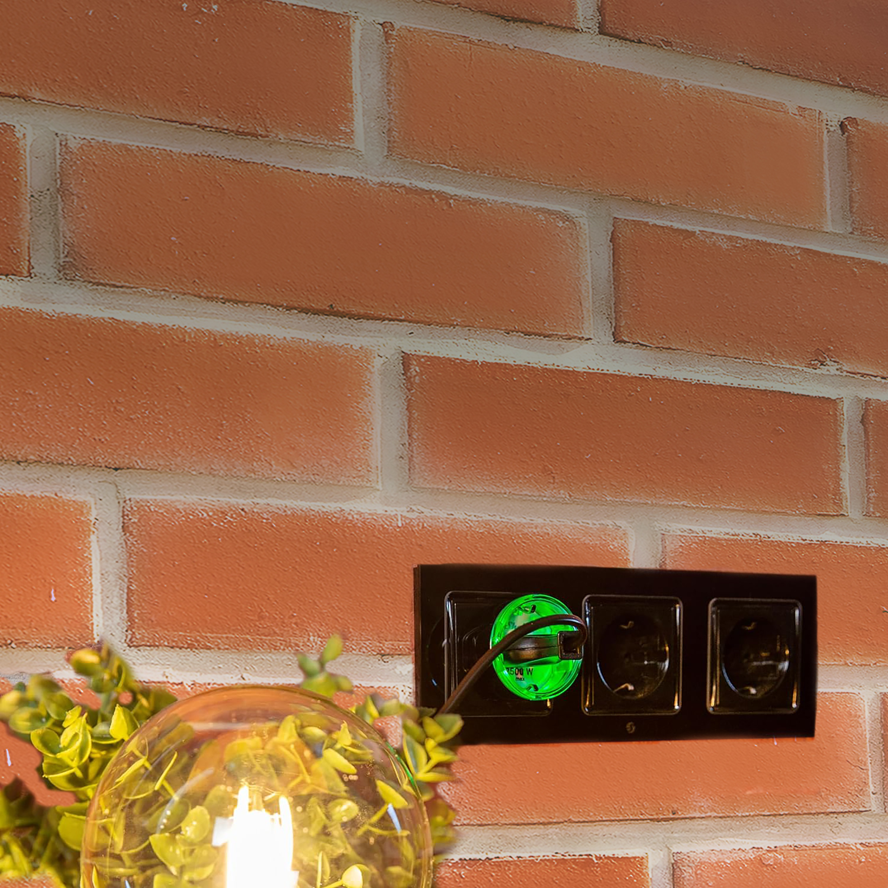Primer plano de una pared de ladrillo con un enchufe eléctrico negro y una luz verde iluminada en su interior.