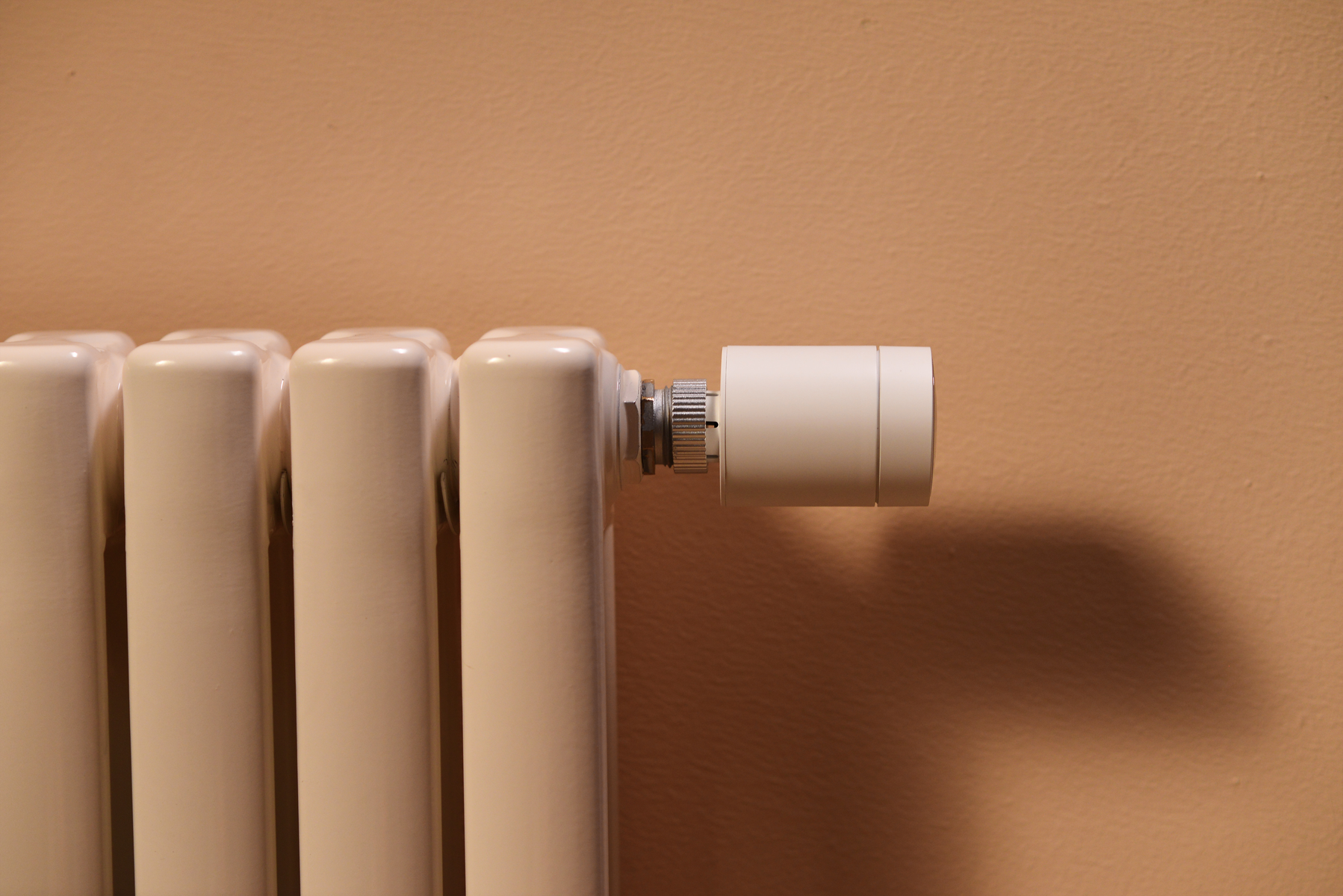 Weißer Heizkörper mit weißem Thermostat. Beiger Wandhintergrund.