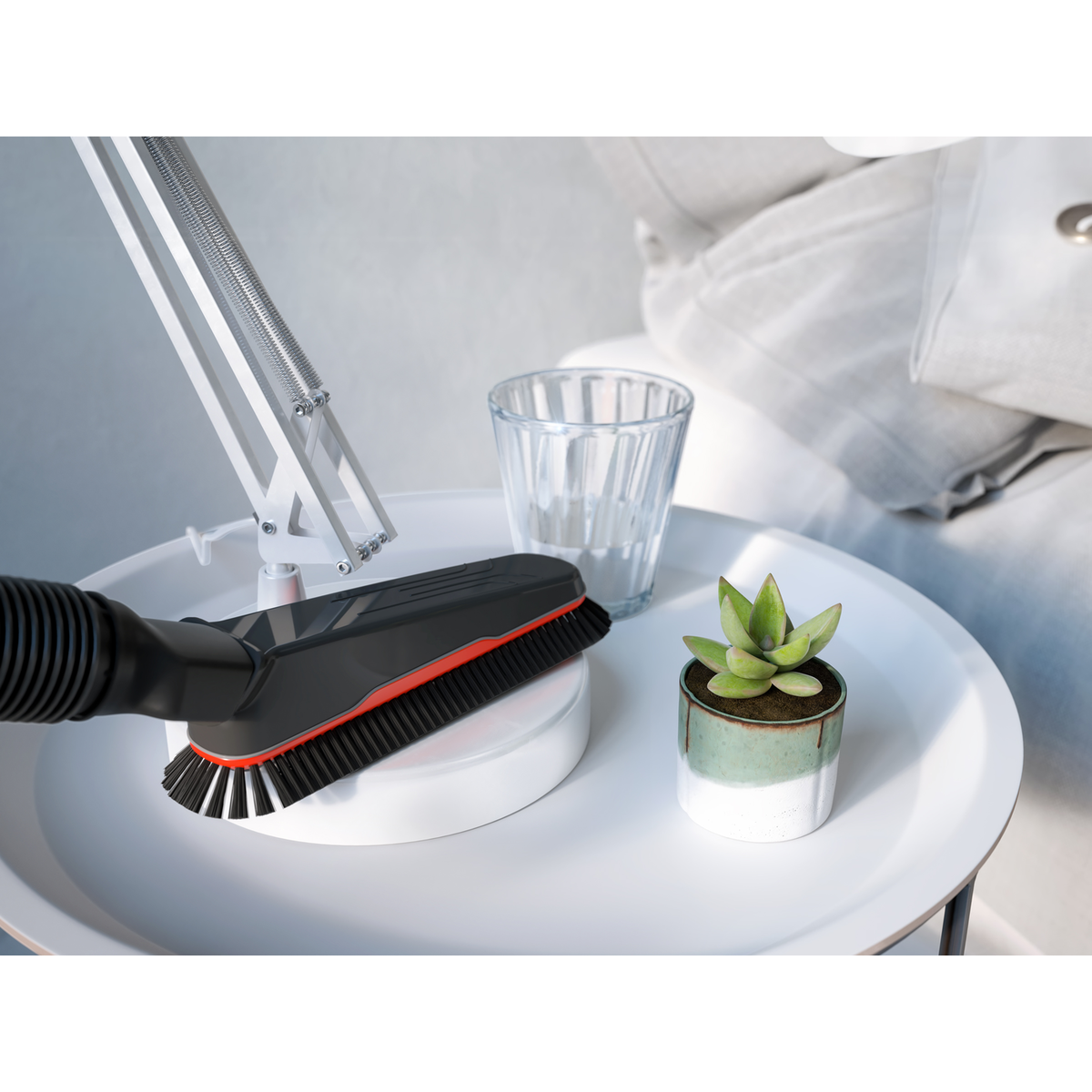 Una testina per aspirapolvere con spazzola, una piccola pianta e un bicchiere su un tavolo bianco.