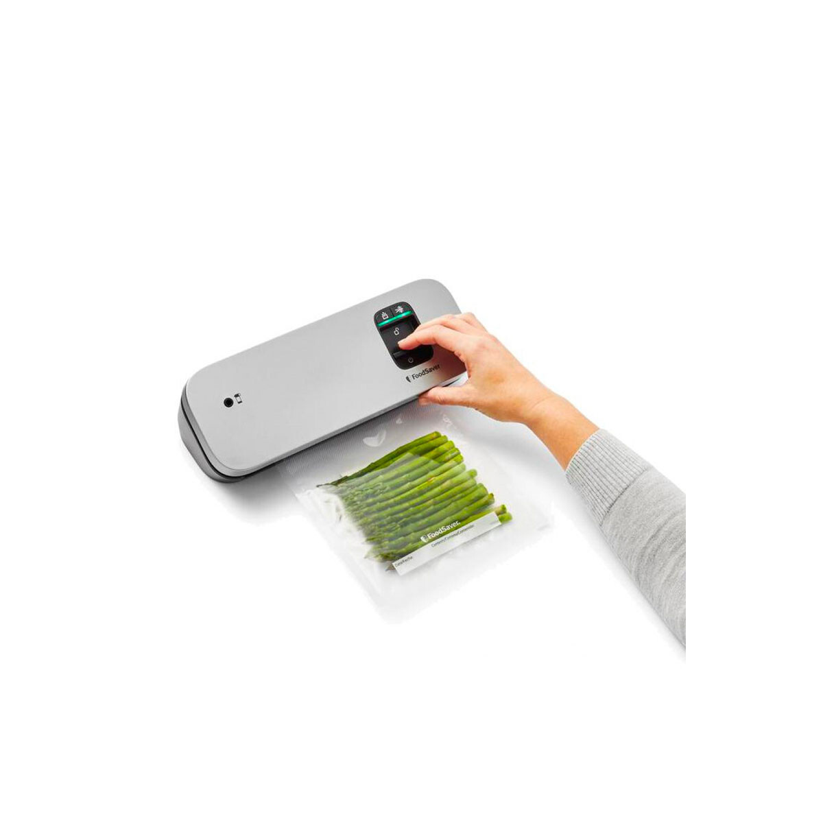 Ein FoodSaver-Gerät mit einer Hand, die den Vakuumverschlussknopf drückt, und einem Beutel Spargel.