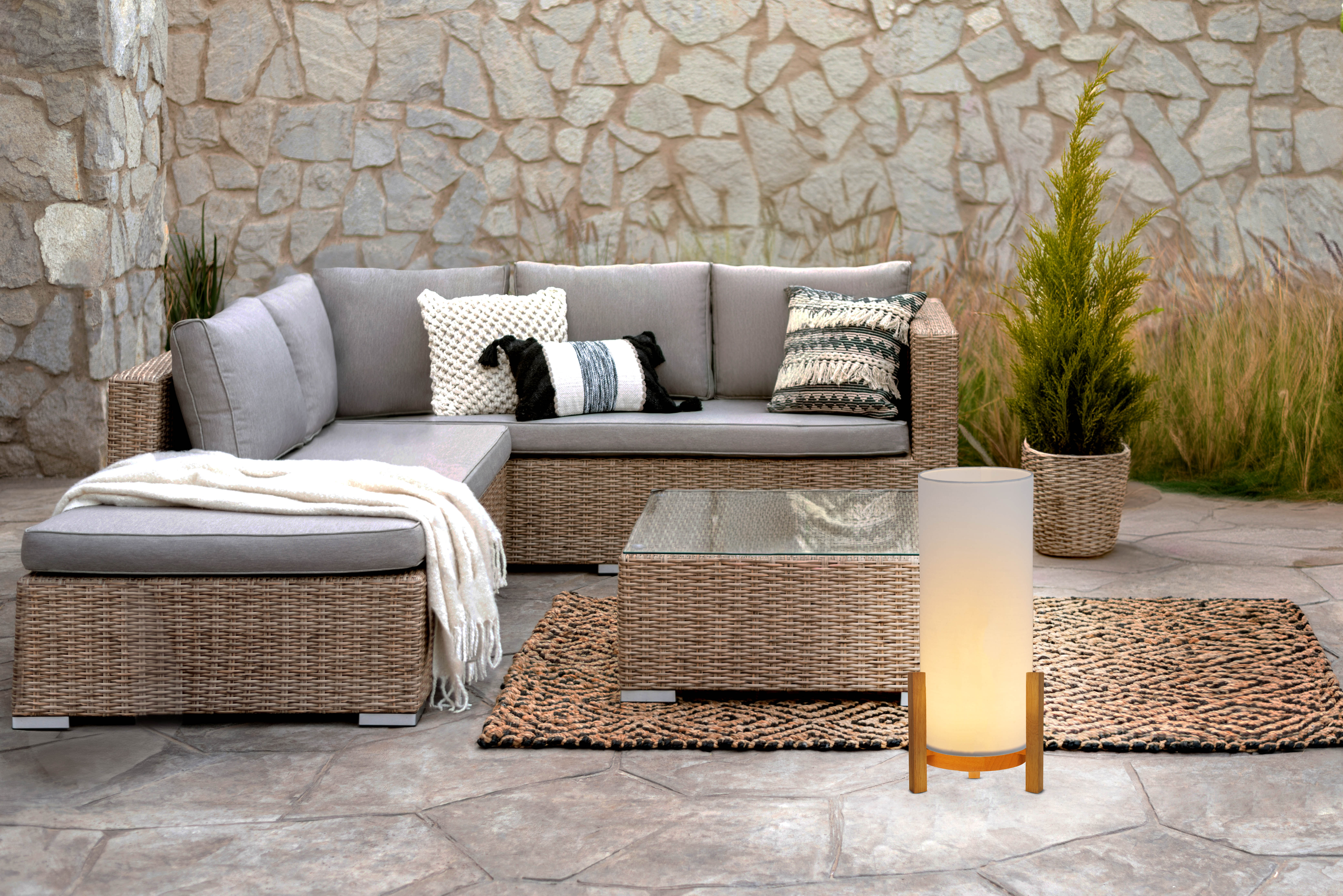 Sitzbereich im Freien mit Sofa, Tisch, Lampe und Teppich auf Steinterrasse.