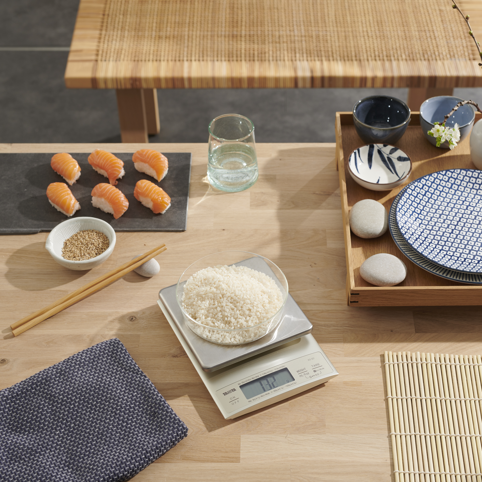 Sushi, rijst in een kom, eetstokjes en borden op een houten tafel met een weegschaal.