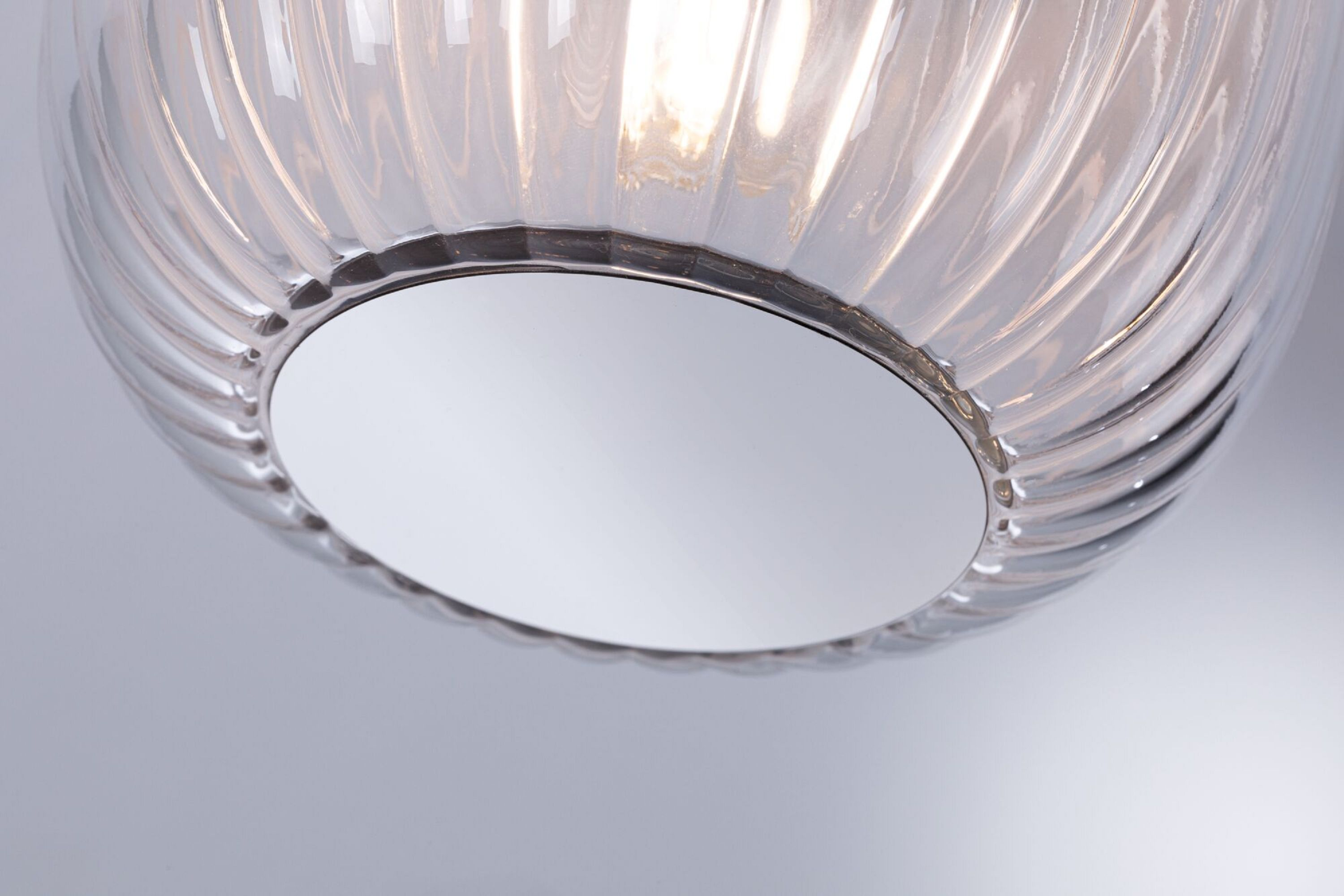 Nahaufnahme einer Glasleuchte mit silbernem Sockel, die Licht aussendet.