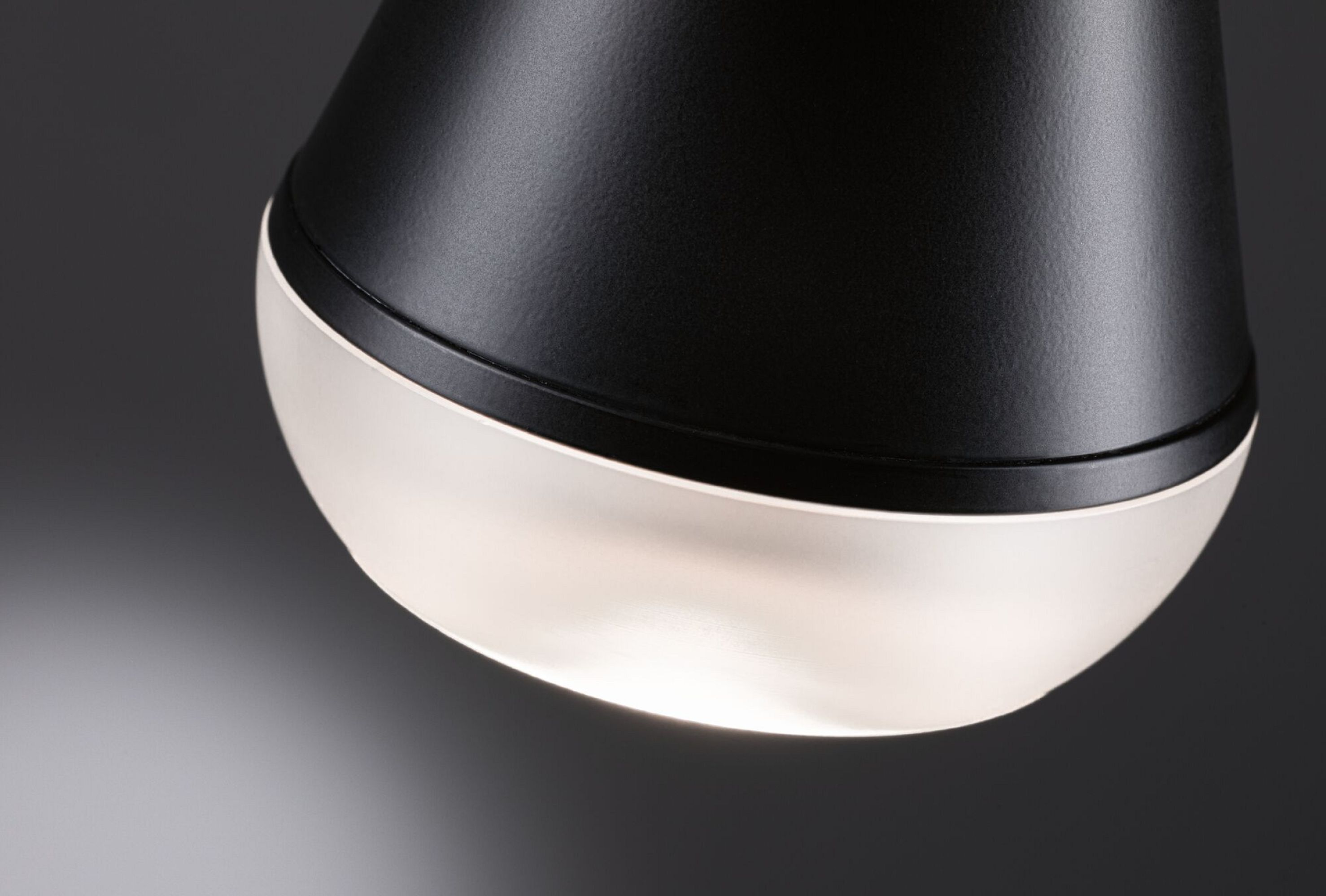 Zbliżenie czarno-białej lampy. Światło świeci od dołu. Czarna lampa sufitowa.