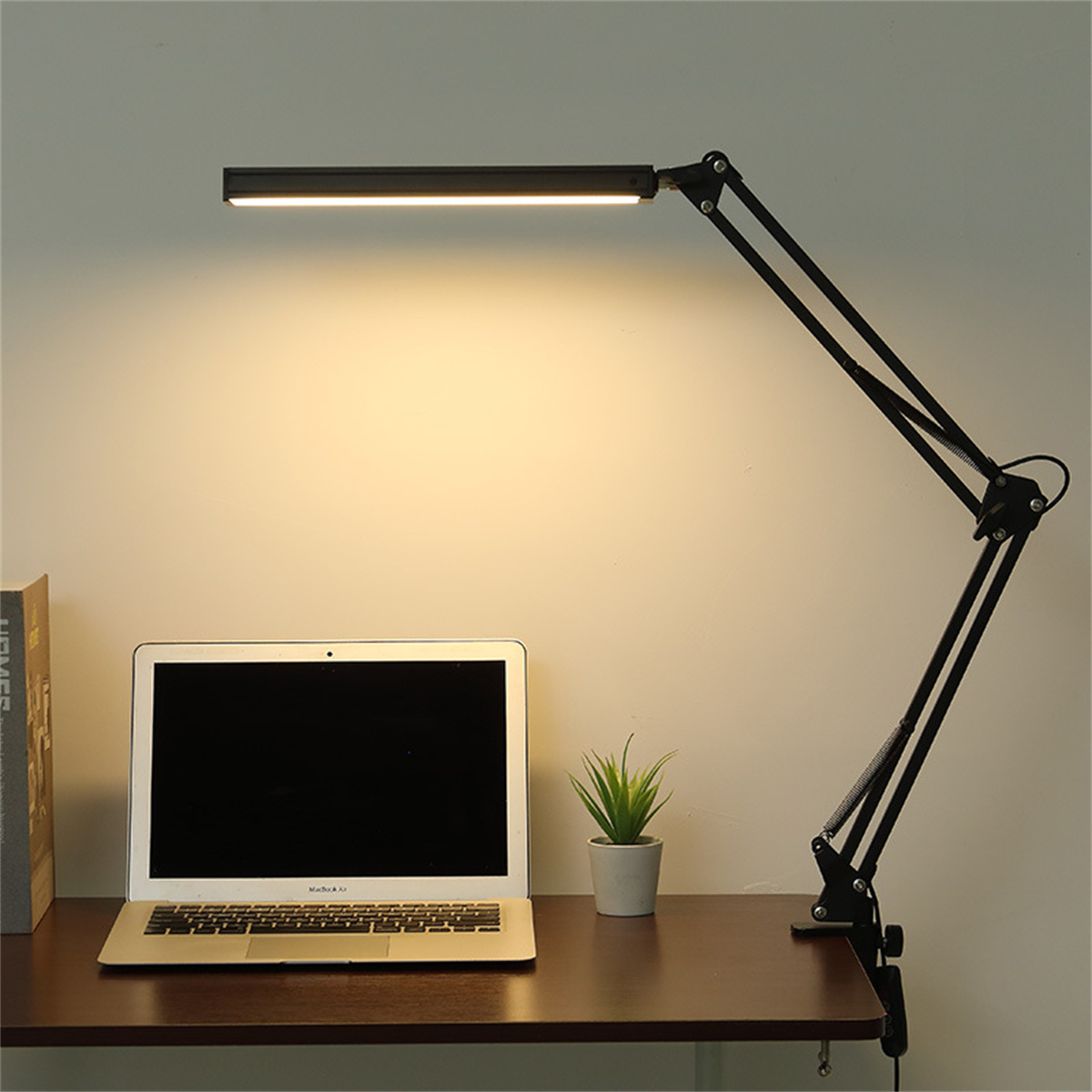 Schwarze Schreibtischlampe über Laptop, Pflanze und Buch.