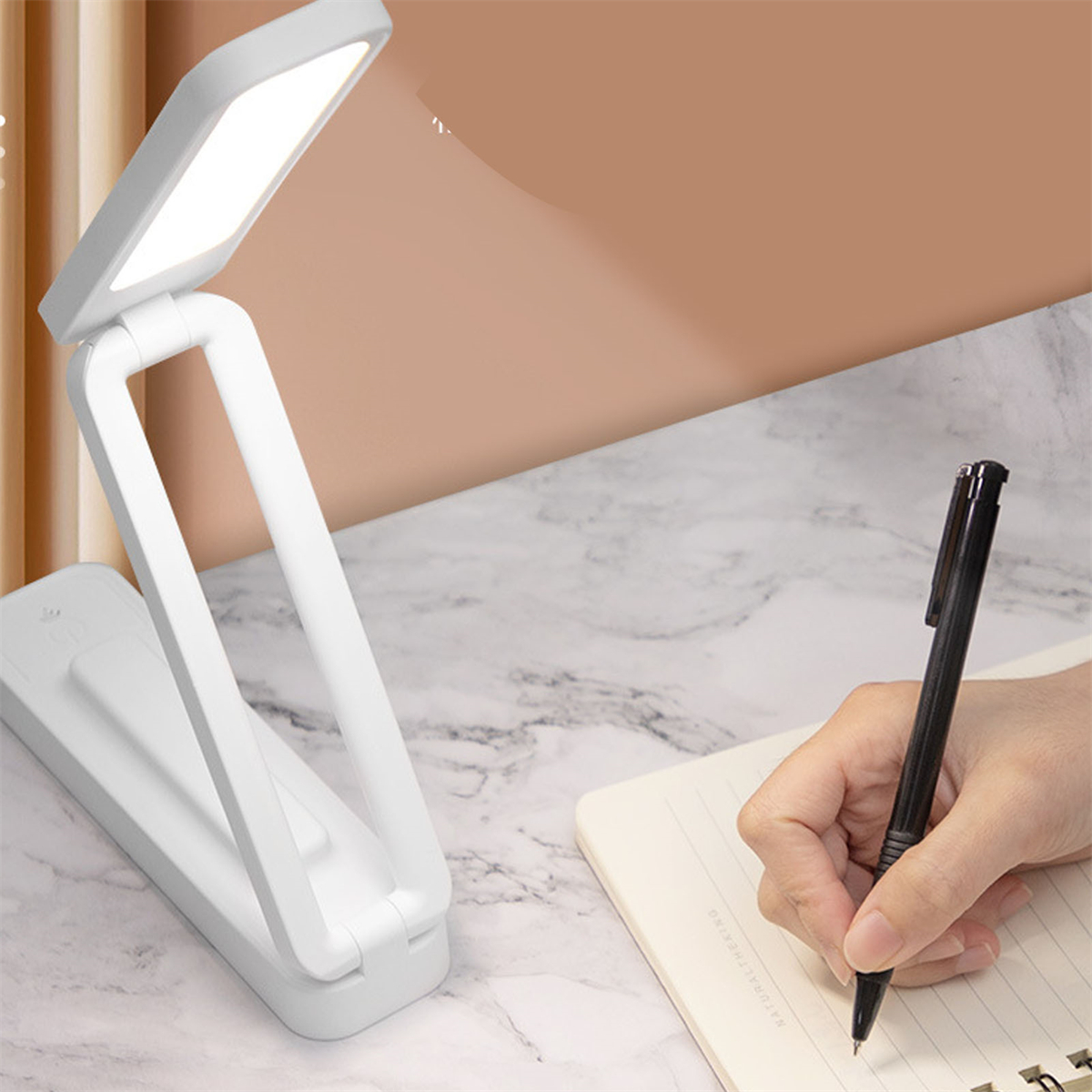 Eine weiße Schreibtischlampe mit LED-Licht, neben einem Stift und einem Notizbuch mit beigem Hintergrund.