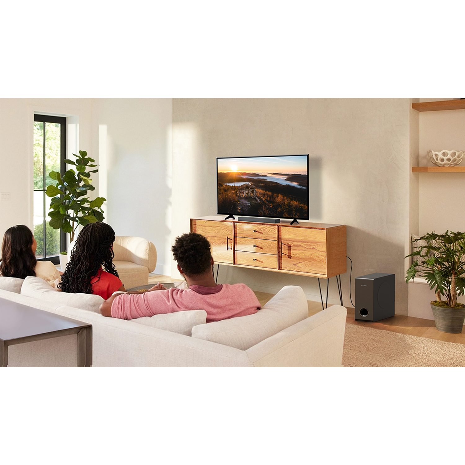 Drei Personen schauen im Wohnzimmer fern. Holzschrank, Subwoofer.