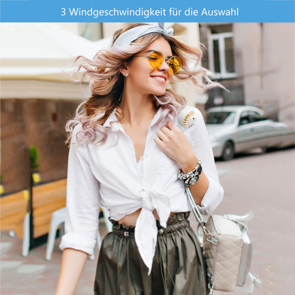 Frau mit Sonnenbrille hält einen kleinen Ventilator draußen an einem sonnigen Tag.