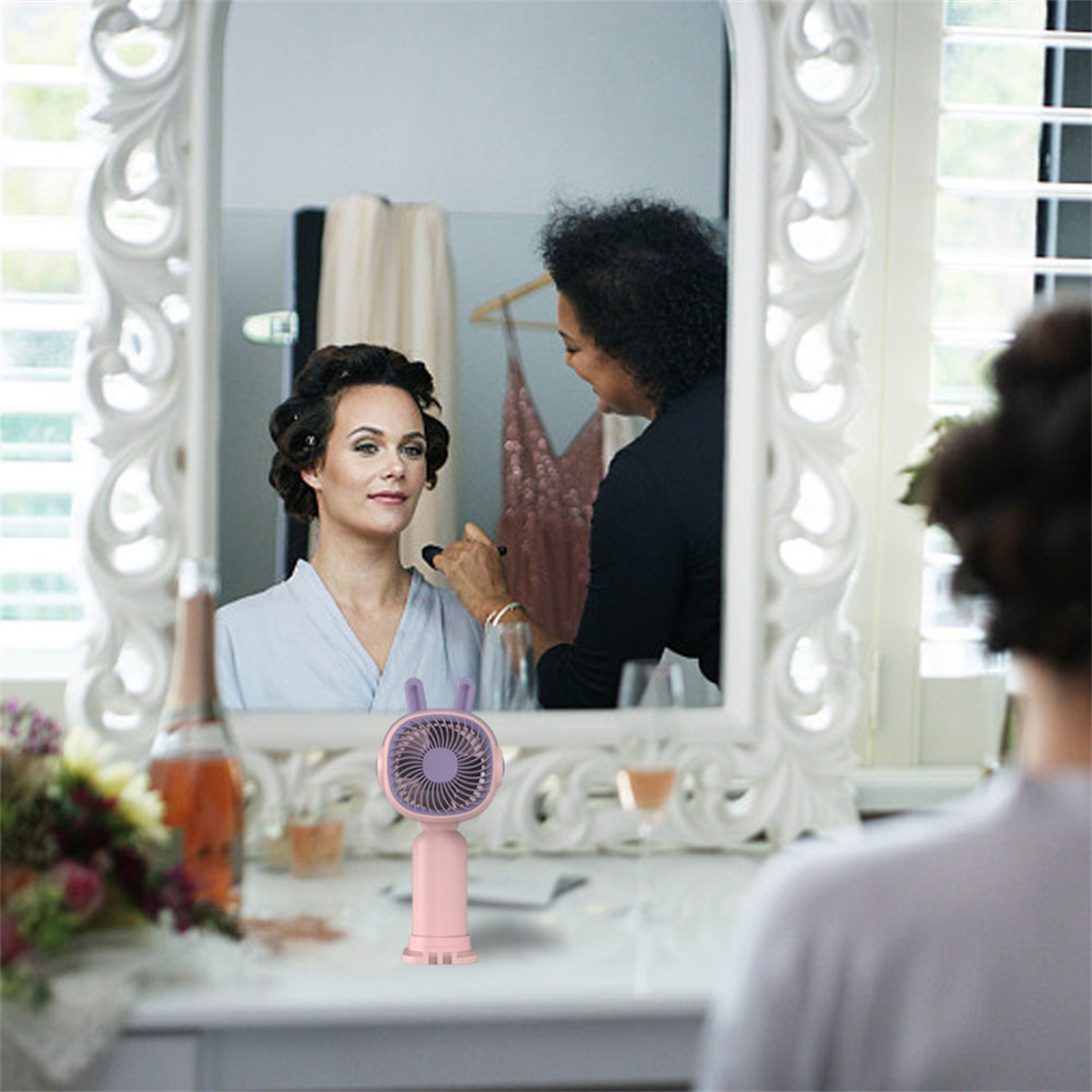 Eine Frau, die sich vor einem Spiegel schminken lässt. Eine Person trägt Make-up mit einem Pinsel auf.