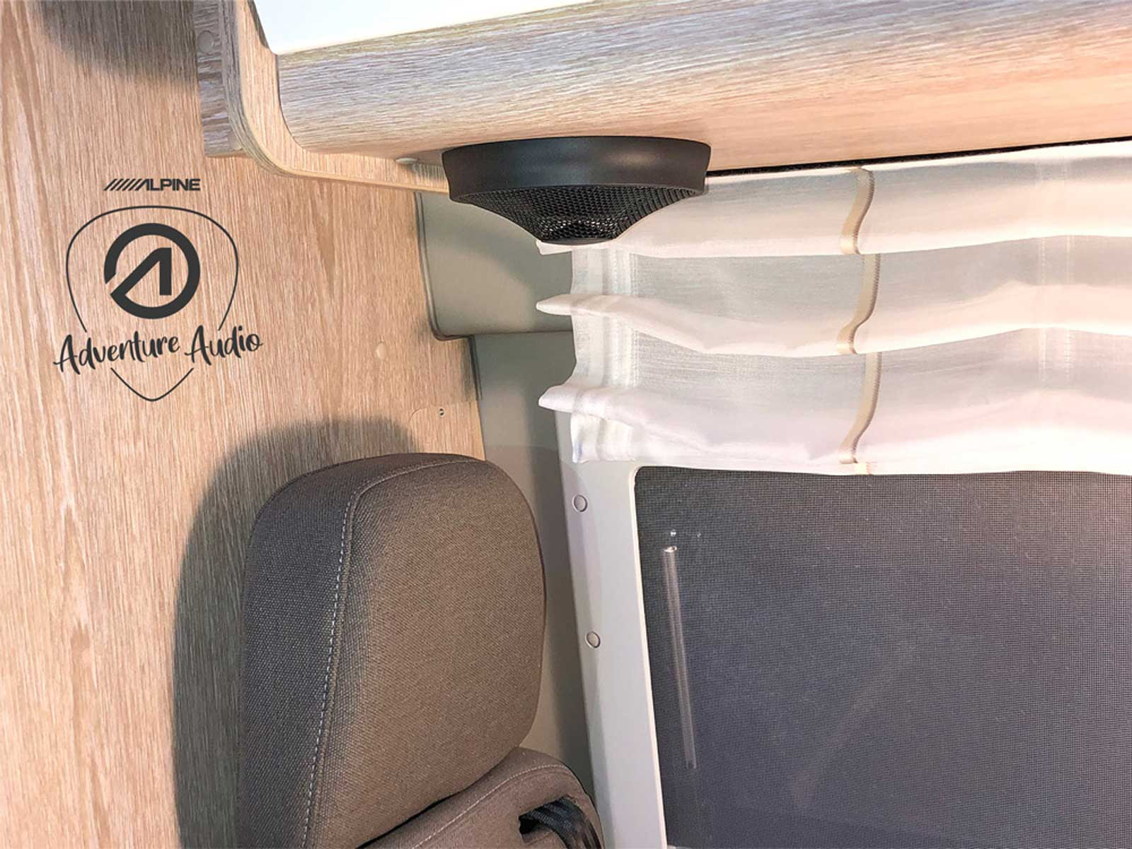 Ein Lautsprecher, der in einem Holzschrank montiert ist. Ein grauer Stuhl und ein Fenster sind im Hintergrund.