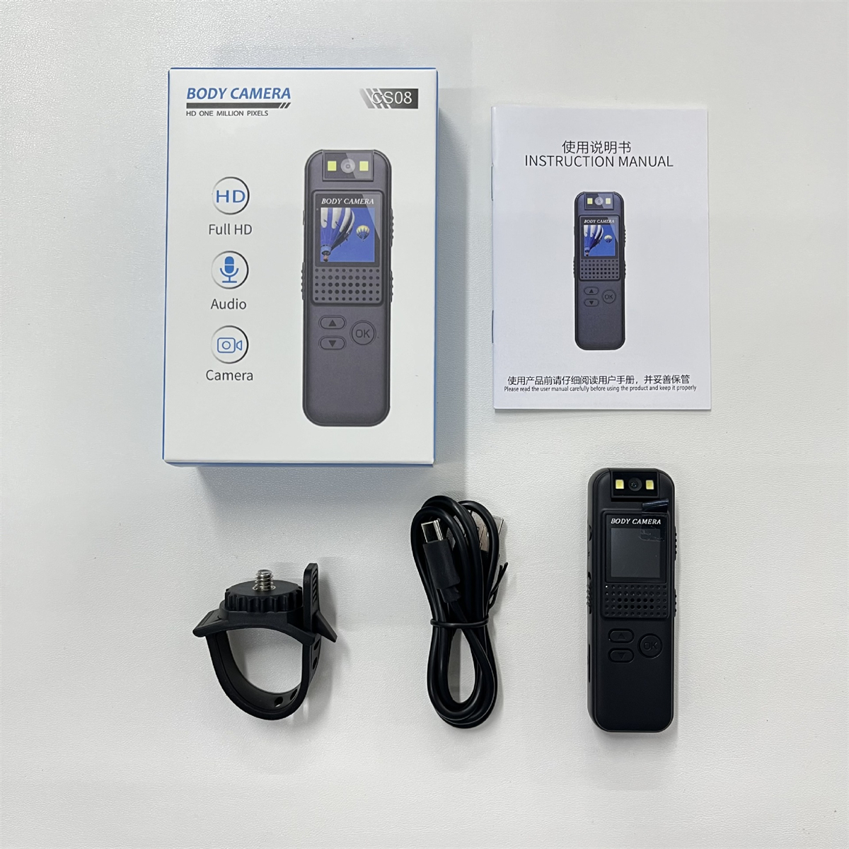 Set aus Körperkamerakomponenten: Kamera, Box, Bedienungsanleitung, Halterung und USB-Kabel, auf weißer Oberfläche ausgelegt.