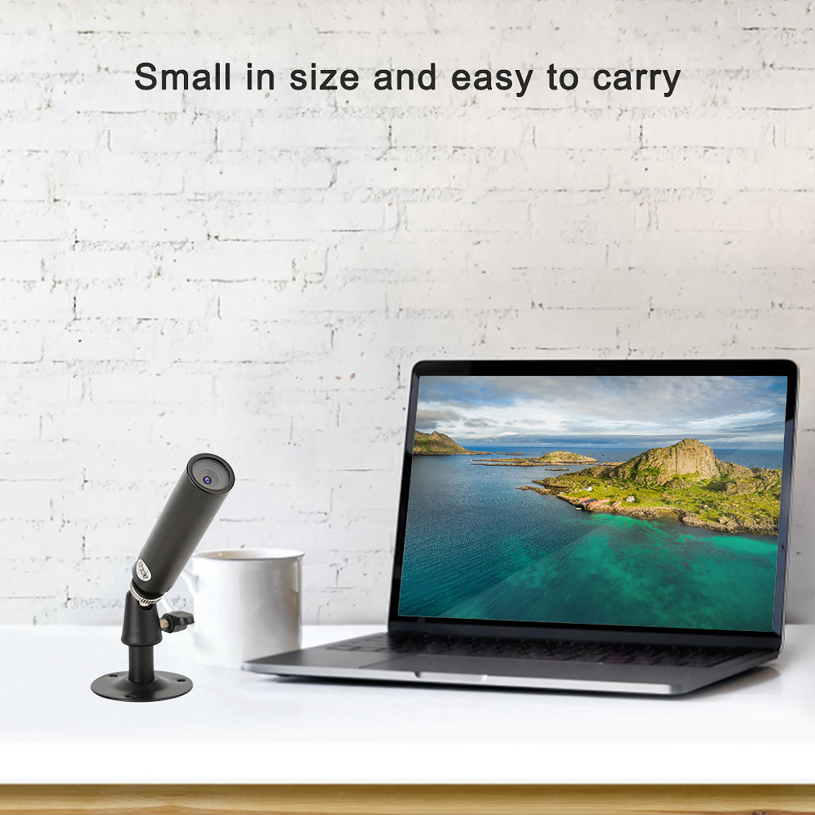 Schwarze Kamera auf weißem Schreibtisch mit Laptop und weißer Backsteinmauer im Hintergrund.