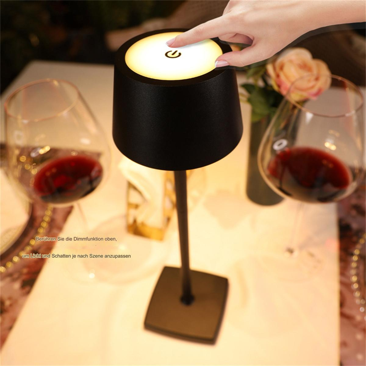 Tischlampe mit Hand, die den Ein-Aus-Knopf berührt, zwei Weingläser mit Rotwein im Hintergrund.