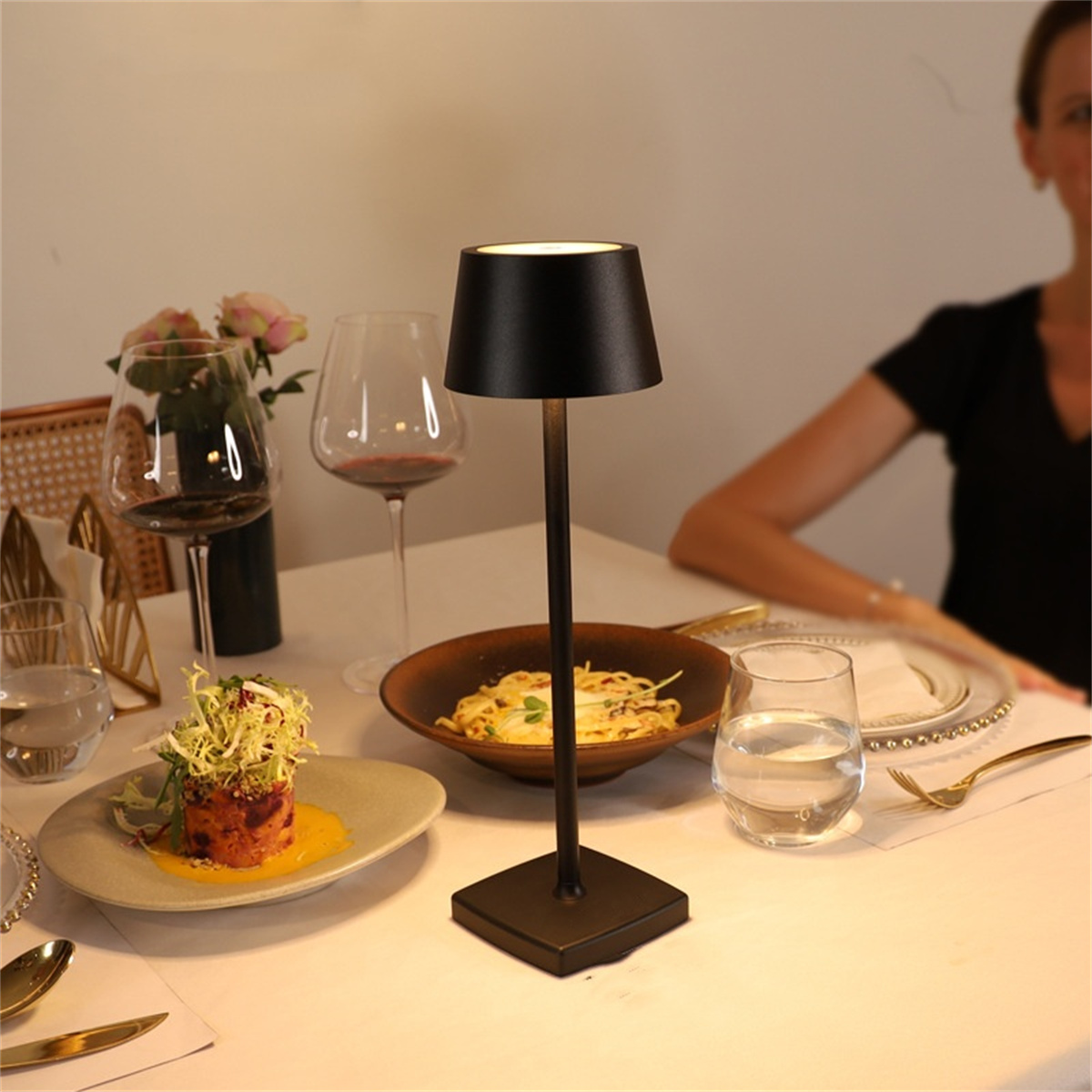 Tischausstattung mit Lampe, Essen, Weingläsern. Eine Frau ist im Hintergrund.