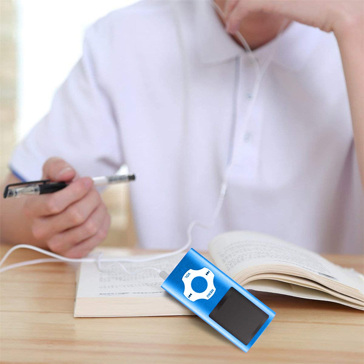 Eine Person hält einen Stift und einen MP3-Player. Ein Buch liegt auf dem Tisch.