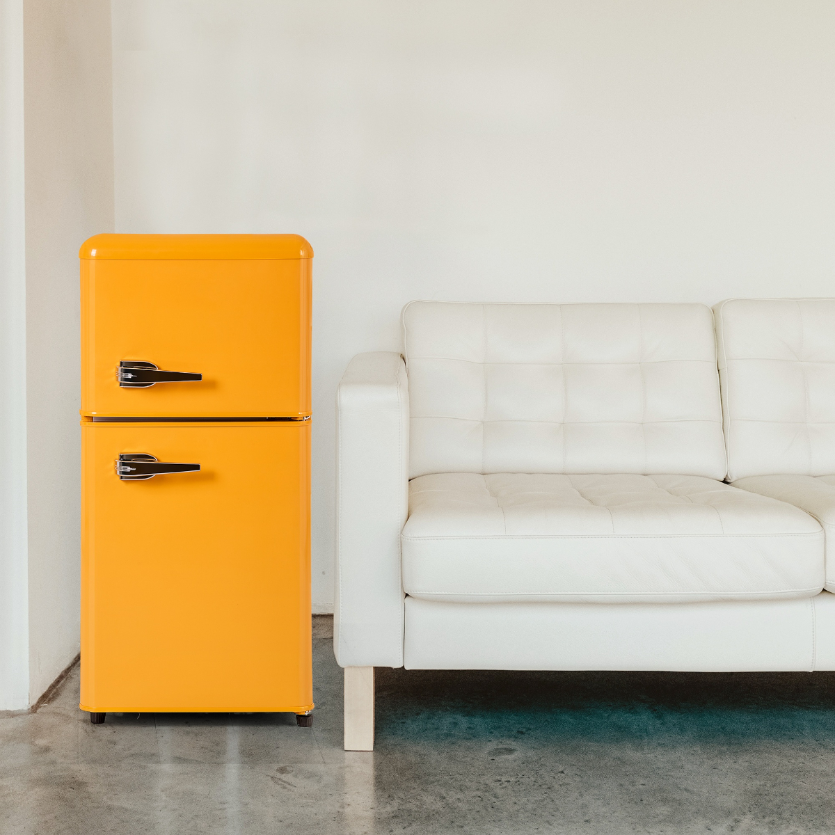 Gelber Retro-Kühlschrank neben einem weißen Sofa auf grauem Betonboden.