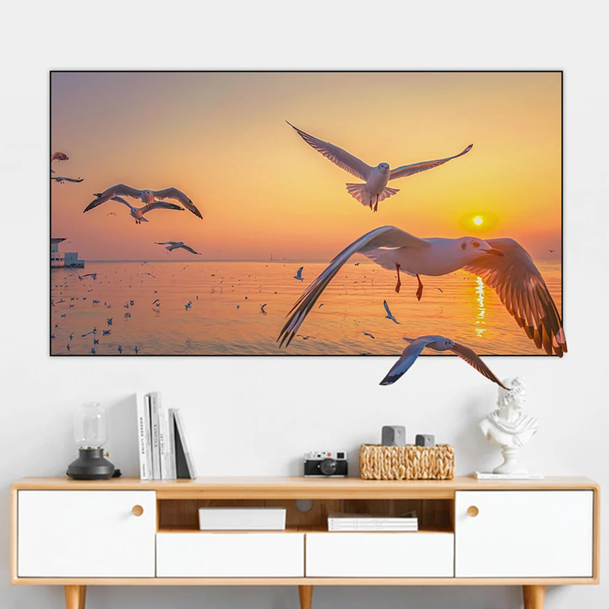 Gaviotas volando sobre el océano al atardecer. El cielo es naranja y amarillo, con una playa al fondo.