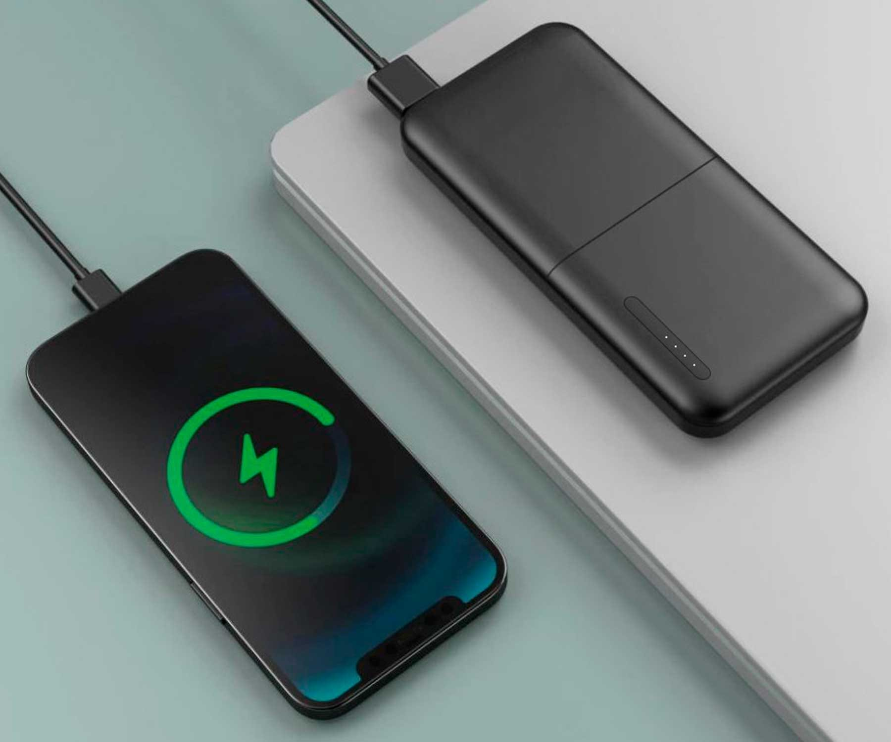 Un téléphone noir se chargeant sans fil sur une surface grise, connecté à une batterie externe noire avec des LED.