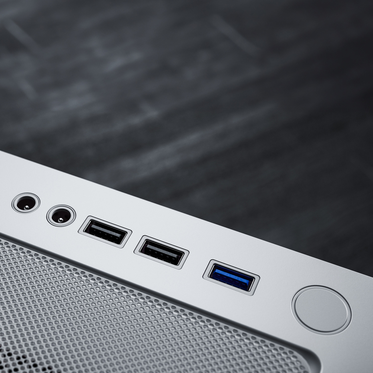 Eine Computercase-Ecke mit USB-Anschlüssen. Sie ist silberfarben mit einem Mesh-Design. Dunkler, verschwommener Hintergrund.