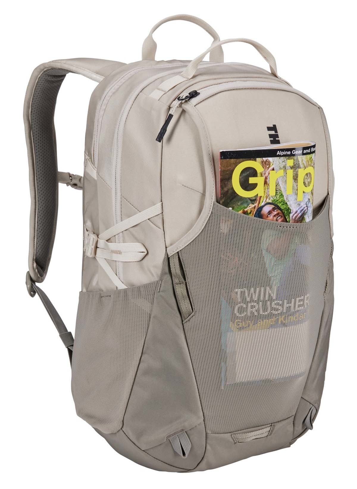 Ein beigefarbener Rucksack mit einer Zeitschrift in der Seitentasche, vor weißem Hintergrund.