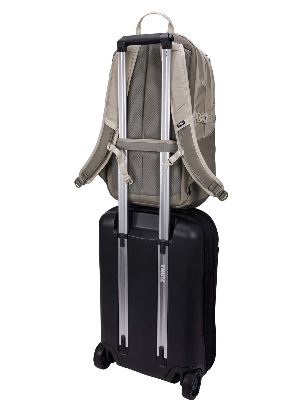Ein beiger Rucksack steht auf einem schwarzen Rollkoffer, vor weißem Hintergrund.