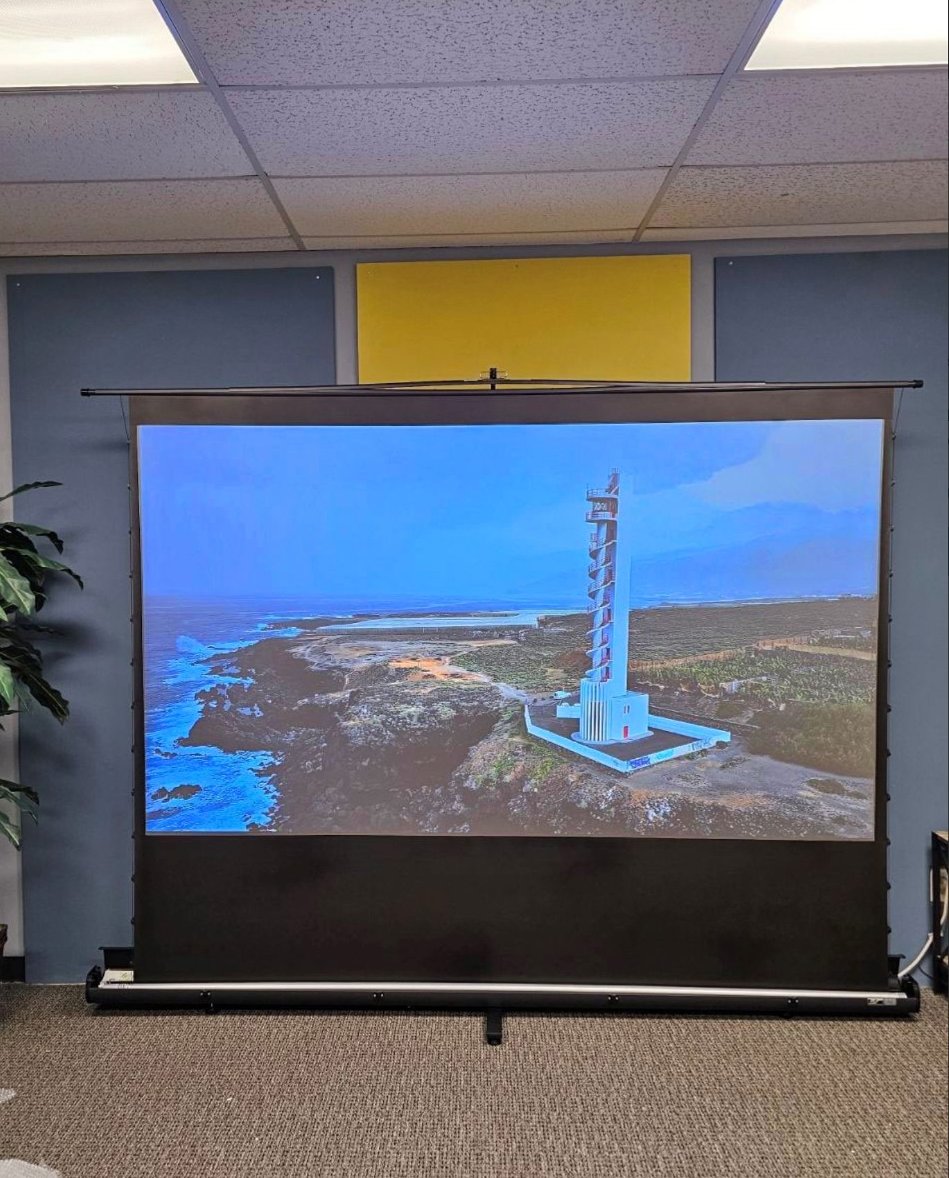 Projectiescherm met een kustscène met een vuurtoren, in een kamer met een grijze muur.