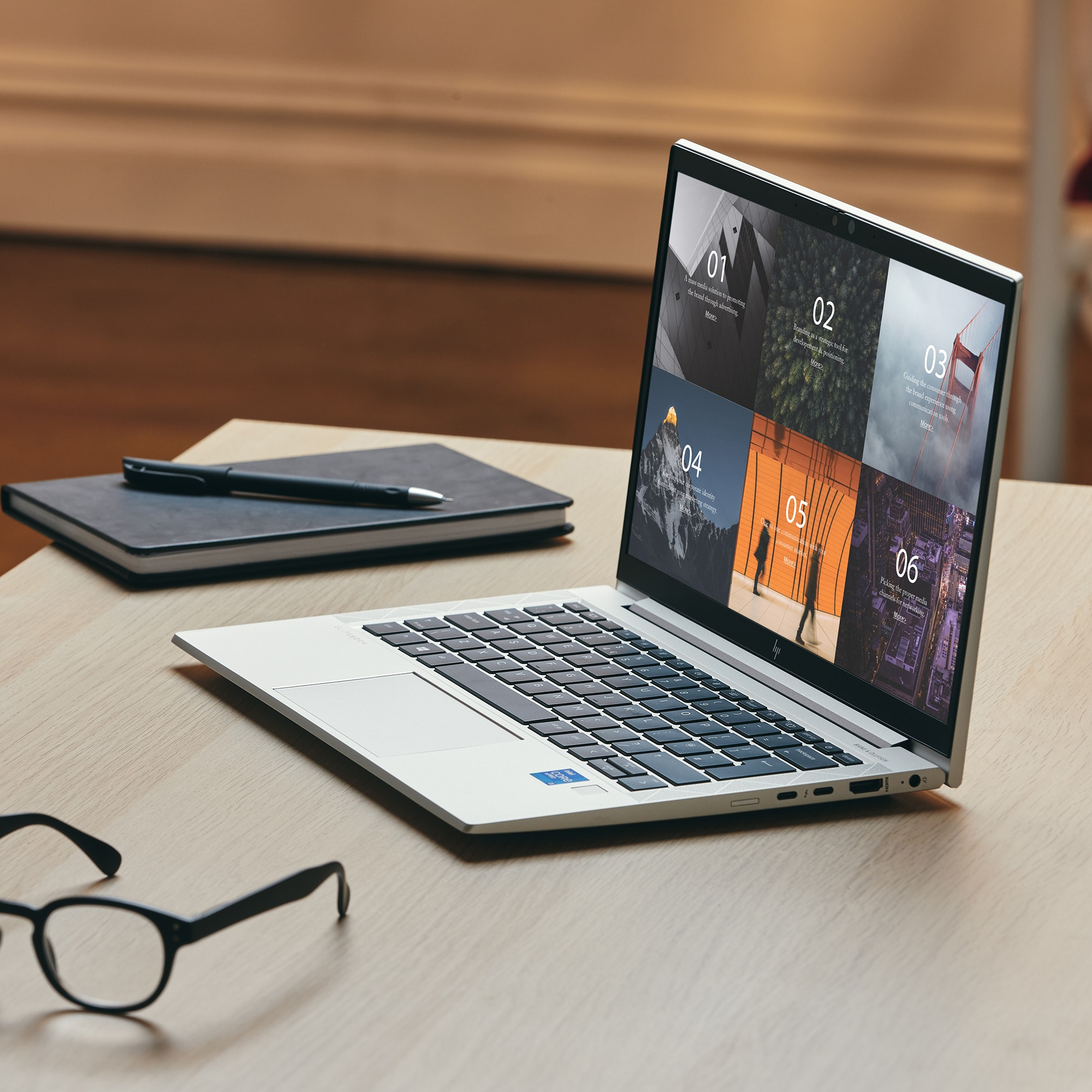 A laptop on a wooden table, with a black notebook and glasses.